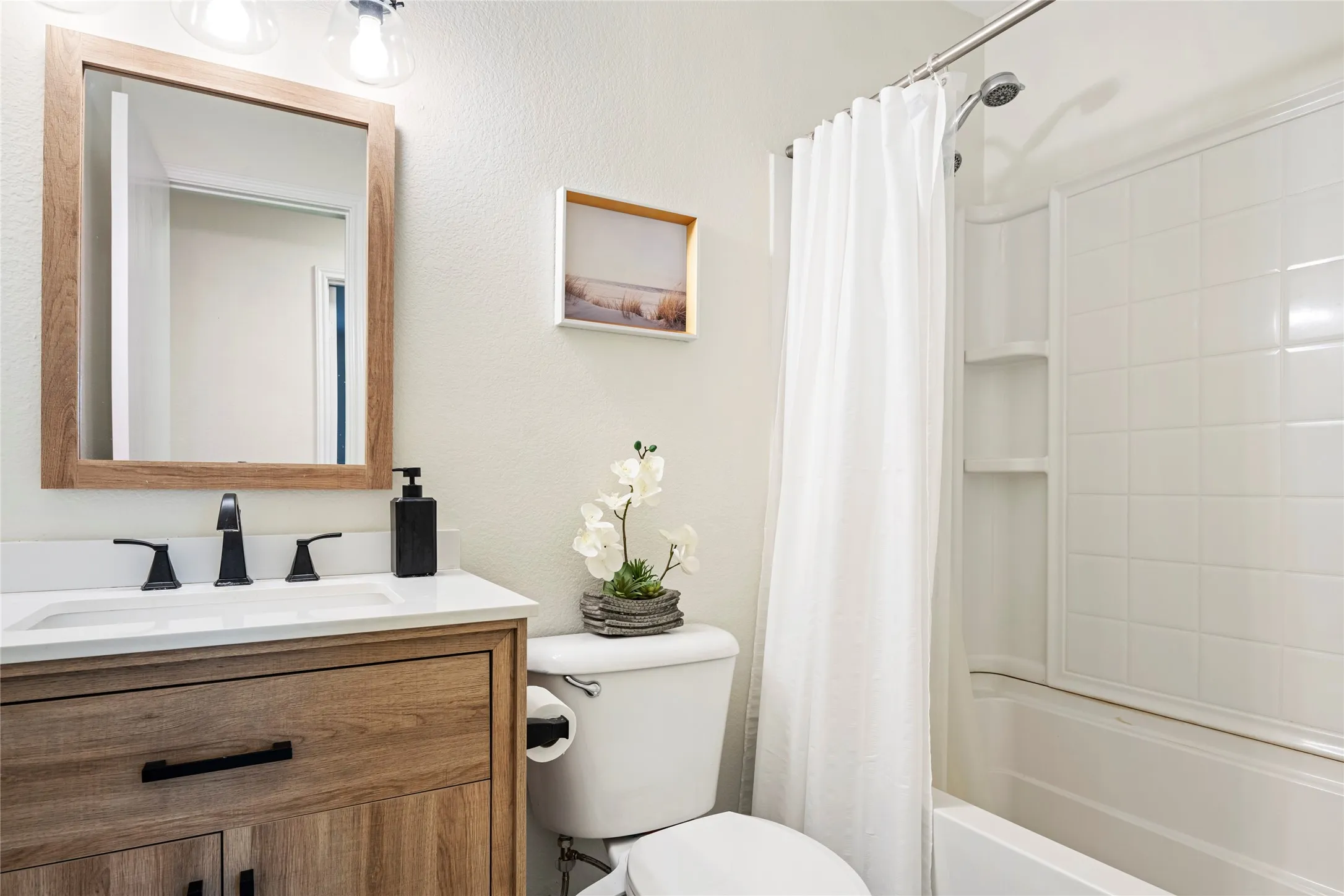 Bathroom featuring a wood-finish vanity with a white countertop and integrated sink, matte black faucet, and a framed mirror