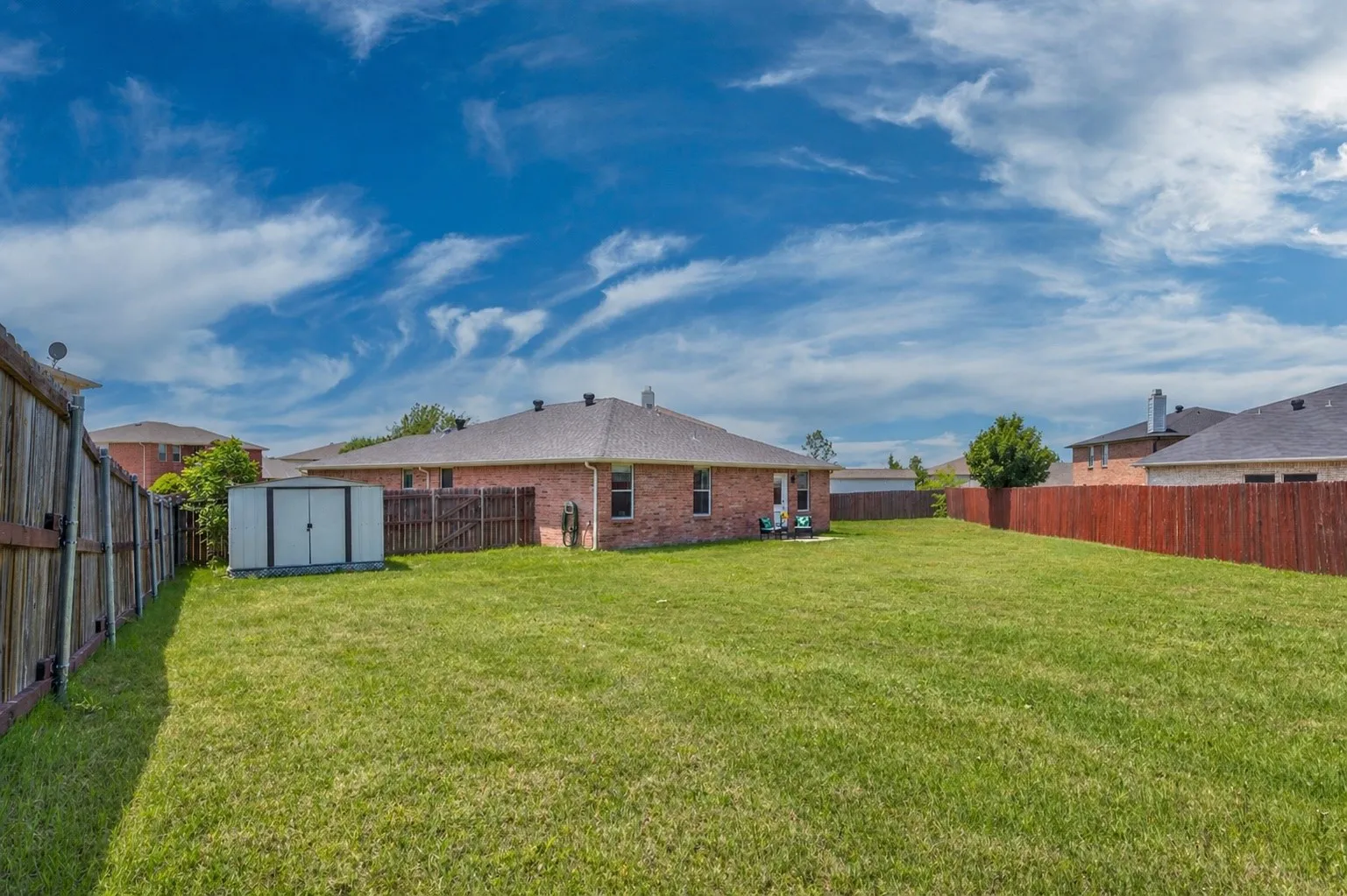 Expansive backyard featuring a manicured lawn, brick exterior, dark shingle roofing, and a storage shed