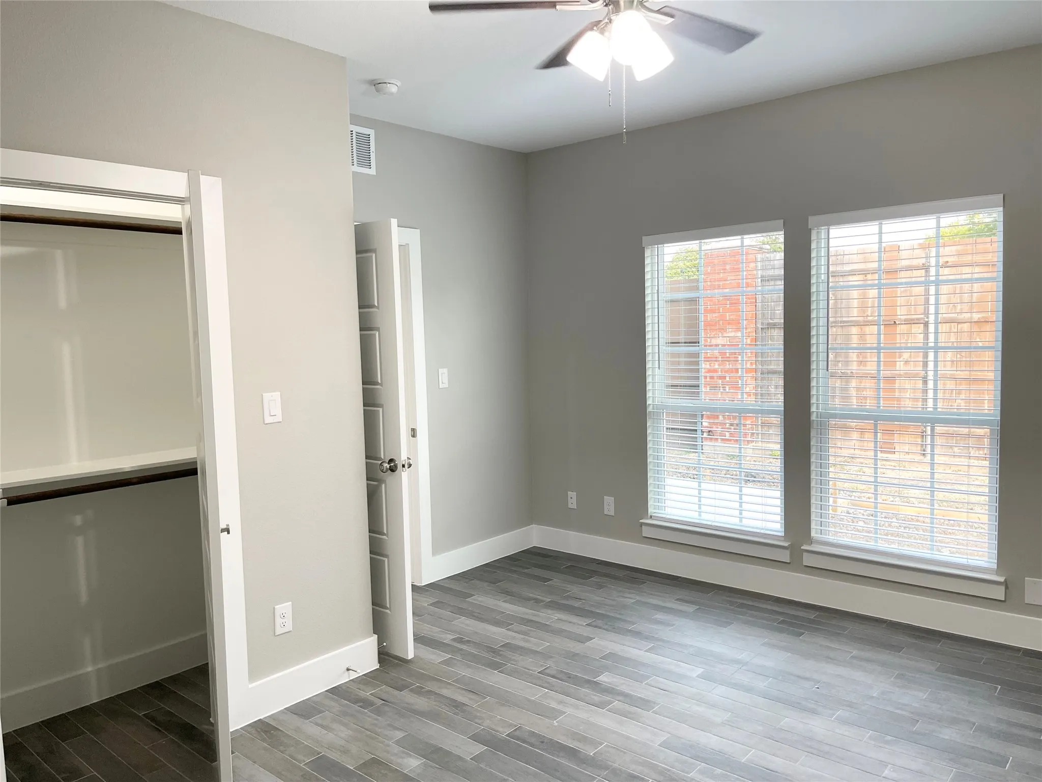 Spacious room featuring wood-finish flooring, light grey walls, white trim, and two large windows with blinds