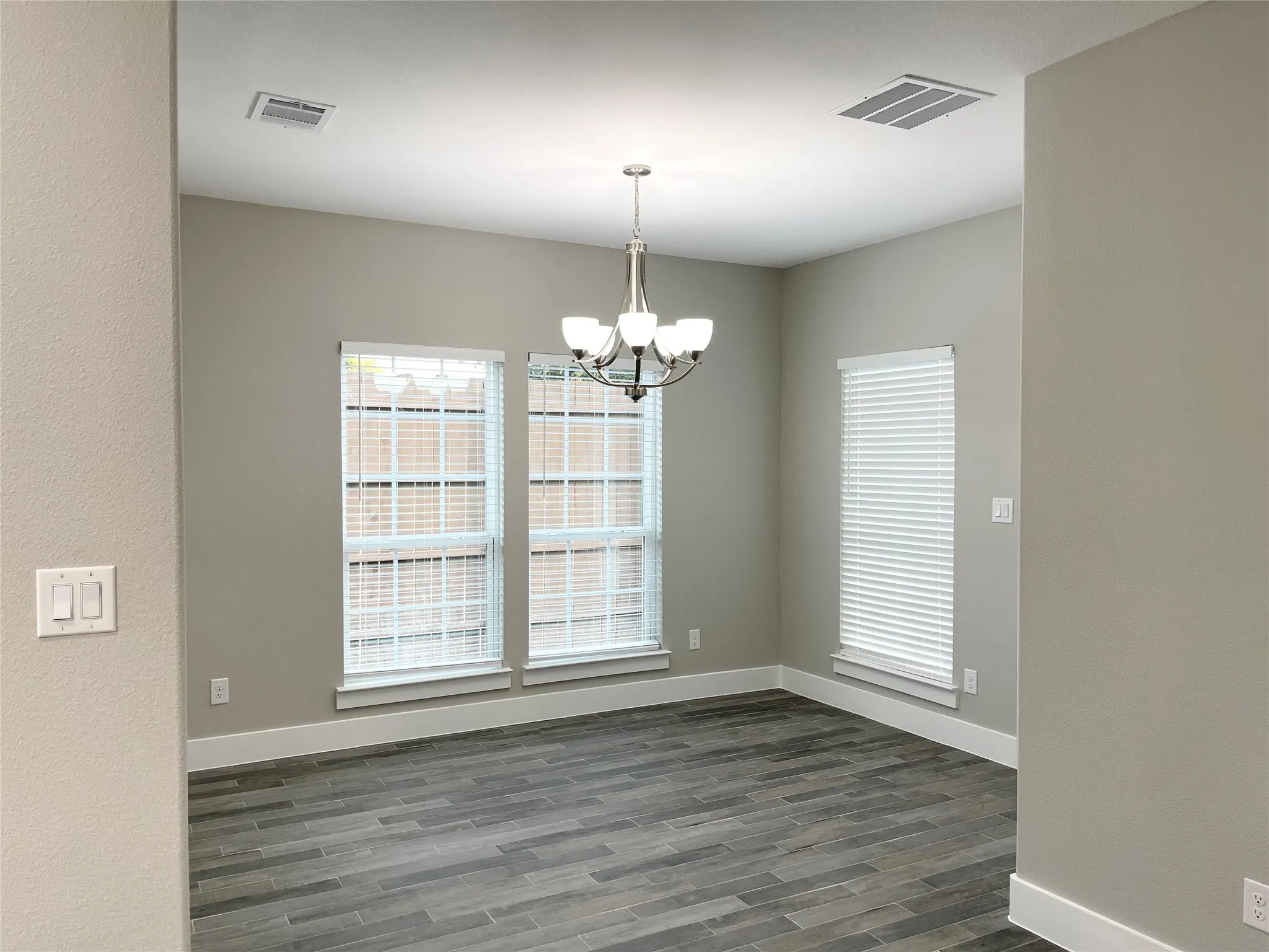 Spacious interior room featuring tile flooring, neutral wall tones, multiple windows with blinds, a ceiling-mounted chandelier, and recessed lighting