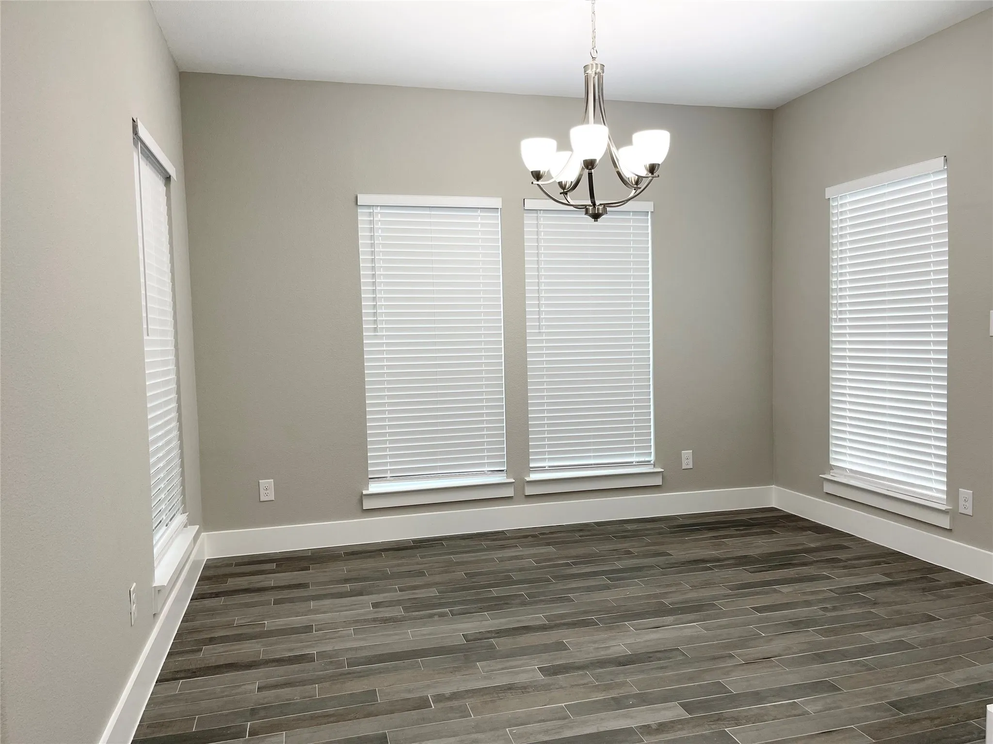 Neutral-toned room featuring a brushed nickel chandelier, tile flooring, multiple windows with blinds, and white trim