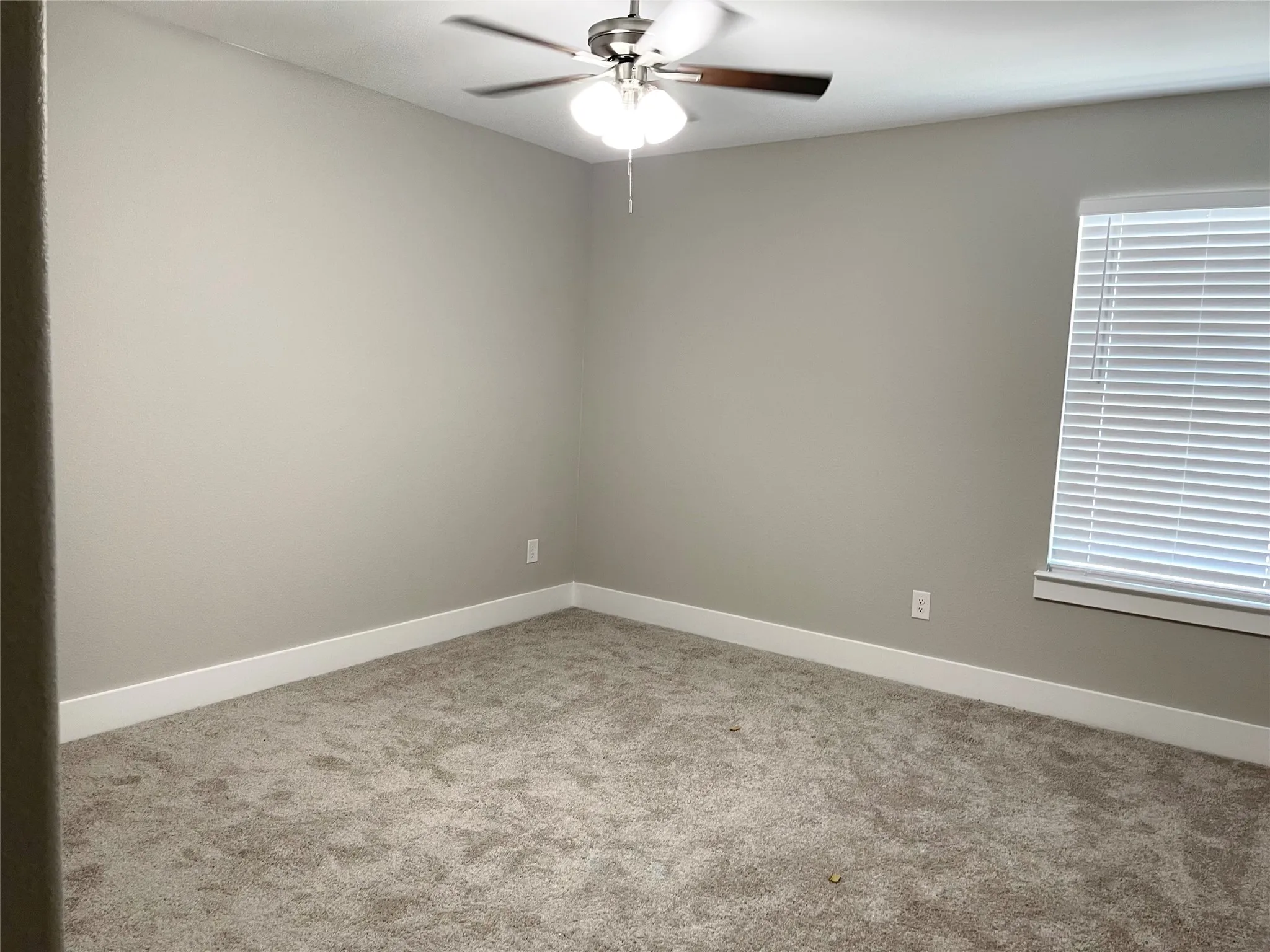 Carpeted interior room featuring light gray walls, white baseboards, and a window with horizontal blinds