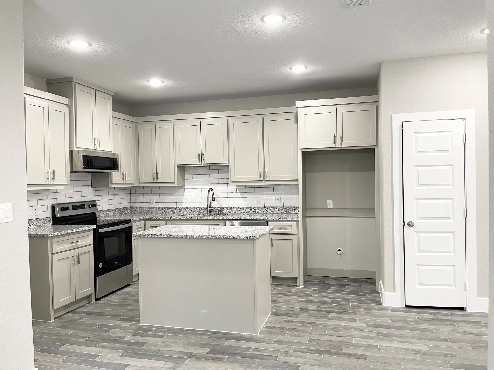 Kitchen featuring light cabinetry, granite-finish countertops, white subway tile backsplash, and a central island