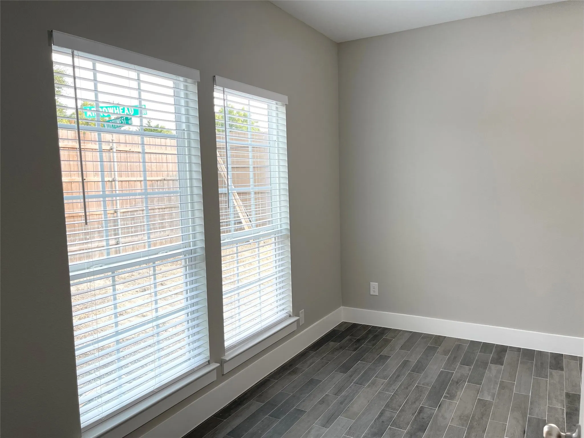 Dual windows with white blinds, wood-finish flooring, light grey painted walls, and white baseboards