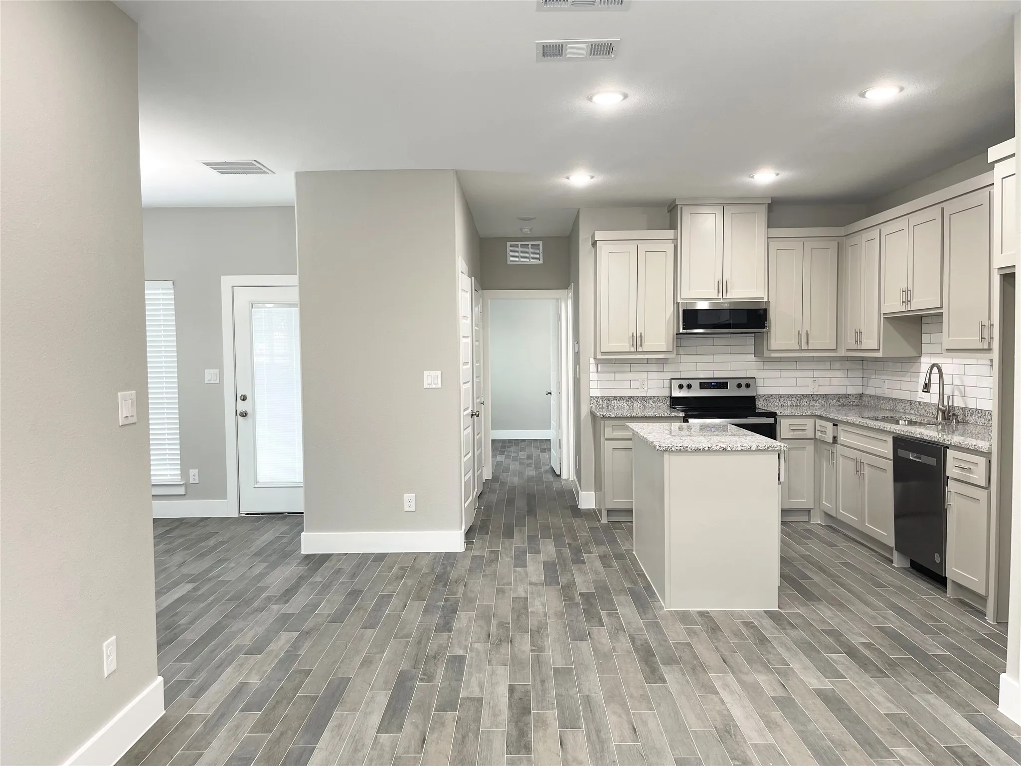Contemporary kitchen featuring white shaker cabinetry, granite countertops, subway tile backsplash, and a central island