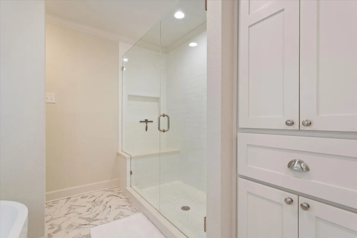 Upstairs glass-enclosed shower with a built-in bench and recessed shelving