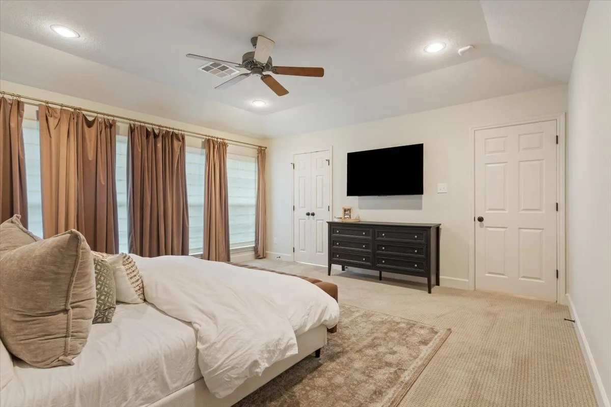 Upstairs carpeted primary suite featuring a tray ceiling with recessed lighting and a ceiling fan