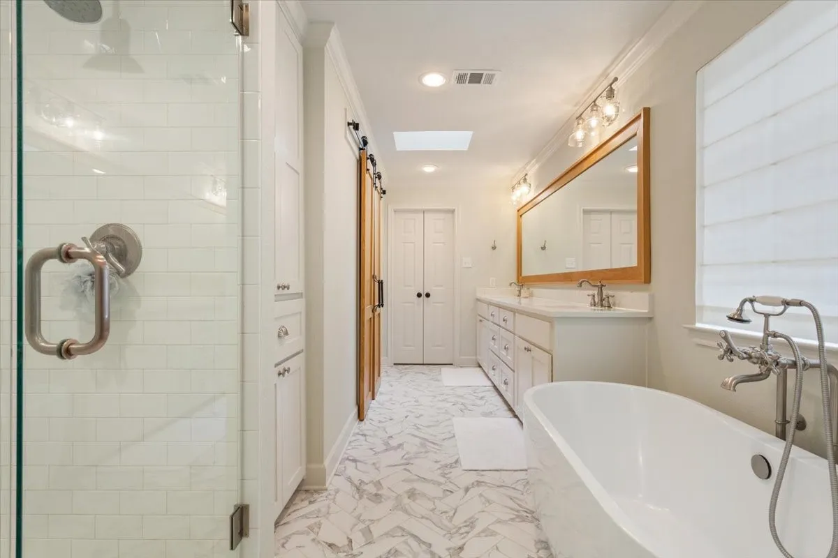 Upstairs freestanding soaking tub with floor-mounted fixture, dual vanity with undermount sinks, and a large framed mirror with overhead lighting