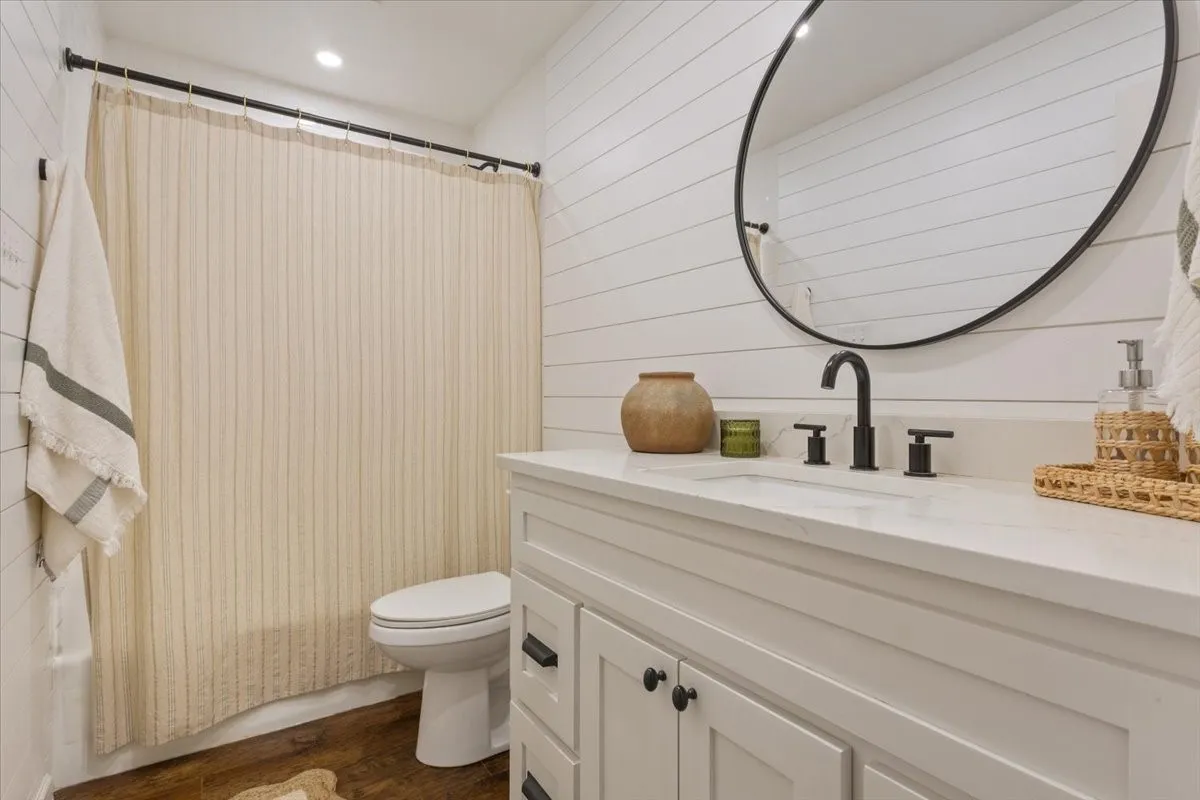 Upstairs bathroom featuring a single vanity with a white countertop, matte black fixtures, an oval mirror, and horizontal shiplap wall paneling