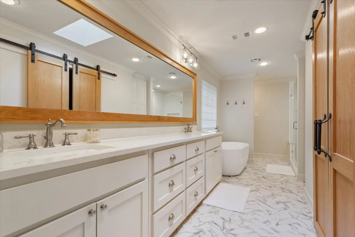 Upstairs bathroom featuring a dual vanity with white cabinetry and light-colored countertops, a freestanding soaking tub, and a glass-enclosed shower
