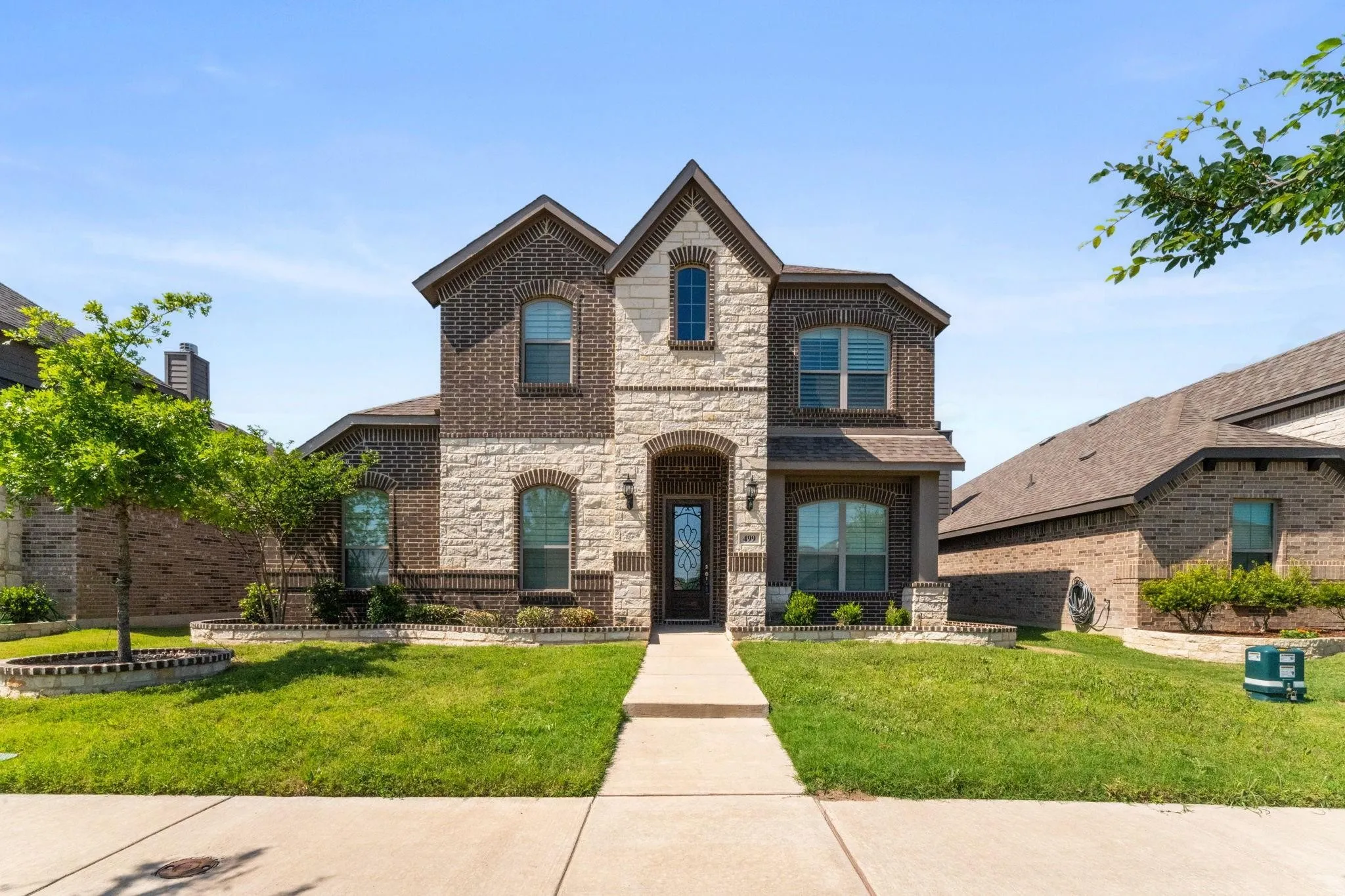 Two-story brick and stone exterior with arched windows, prominent gabled rooflines, and a covered front entry