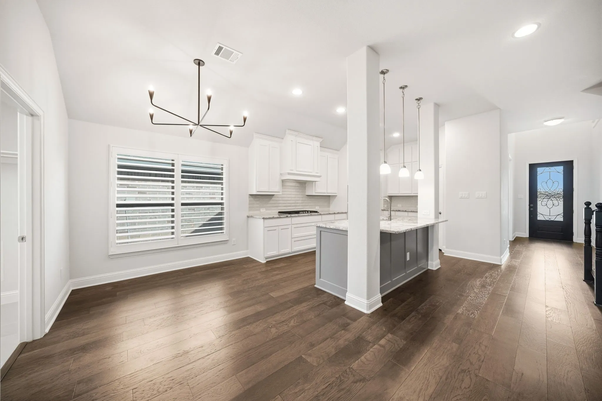 Open-concept kitchen and dining area featuring wood-finish flooring, white cabinetry, an eat-at island with pendant lighting, and a decorative front door