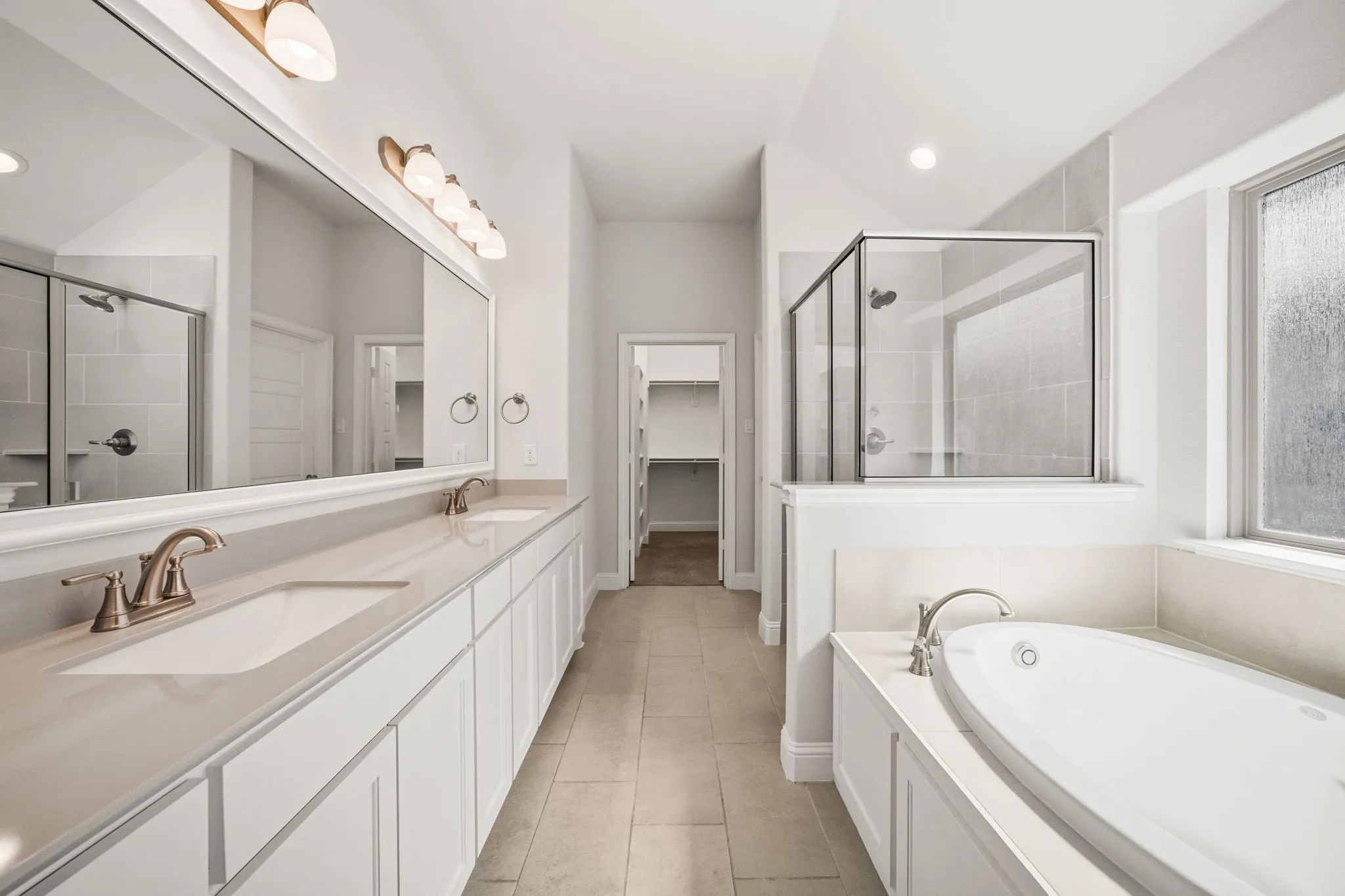 Spacious bathroom featuring a dual vanity with light countertops, separate shower with glass enclosure, soaking tub, and tile flooring
