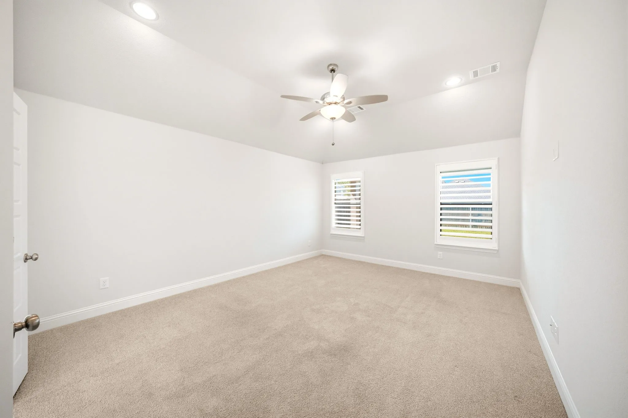 Spacious room featuring vaulted ceilings, recessed lighting, neutral carpet, two windows with blinds, and a ceiling fan with integrated lighting