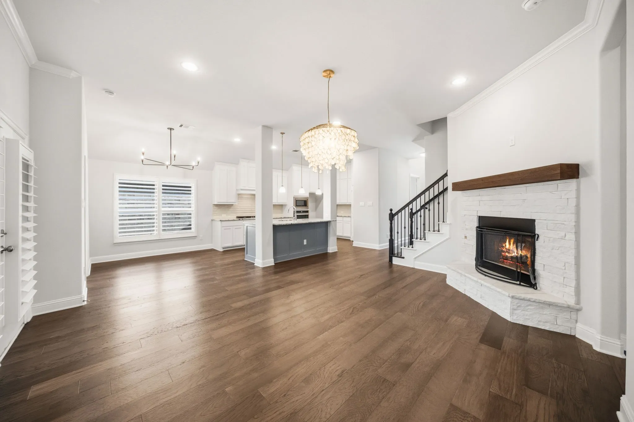 Spacious interior featuring wood-finish flooring, a white brick fireplace with a wood mantle, and an open-concept kitchen with a gray island