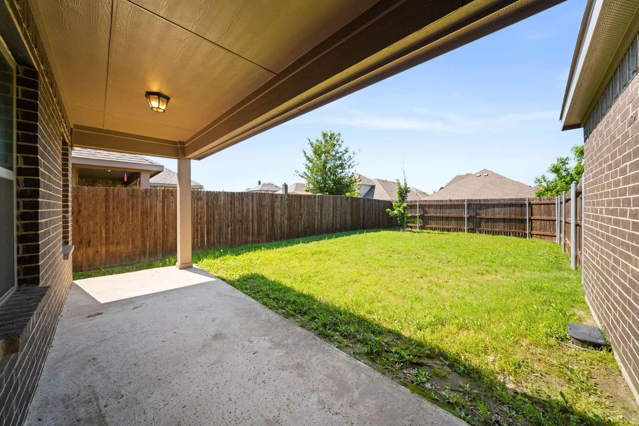 Covered patio with concrete flooring, recessed lighting, brick exterior wall, and direct access to a grassy yard featuring a wood privacy fence