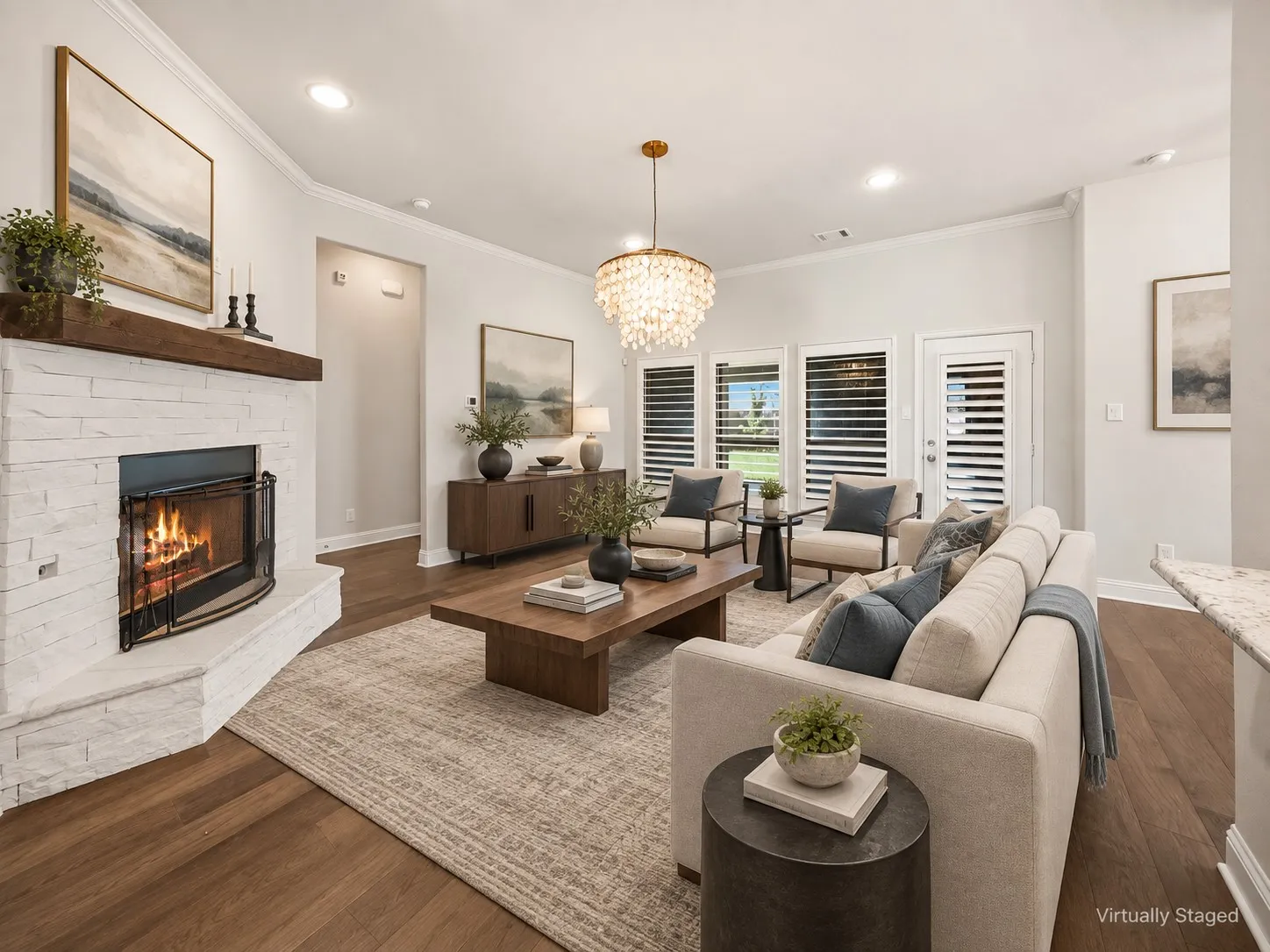 Spacious interior room featuring wood-finish flooring, a white stacked stone fireplace with a wood mantel, and multiple windows with plantation shutters