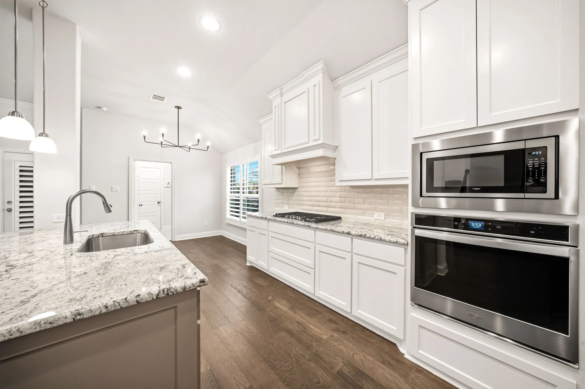 Open-concept kitchen featuring an island with a stainless steel sink, a built-in oven and microwave, white cabinetry, granite countertops, and wood-finish flooring