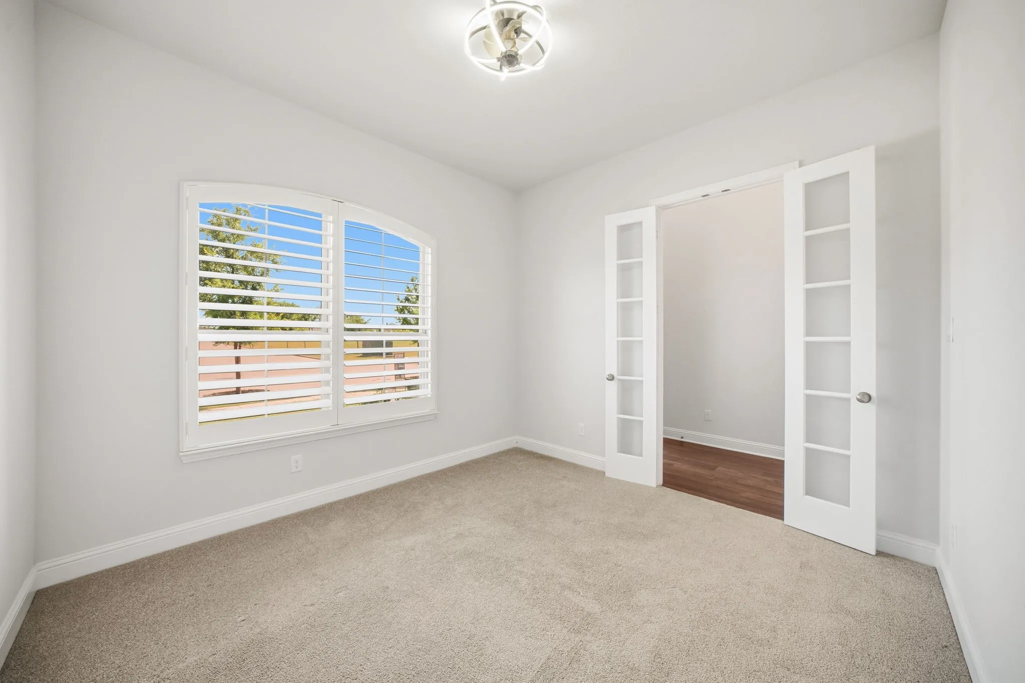 Office featuring an arched window with plantation shutters, carpet flooring, and a contemporary ceiling light fixture