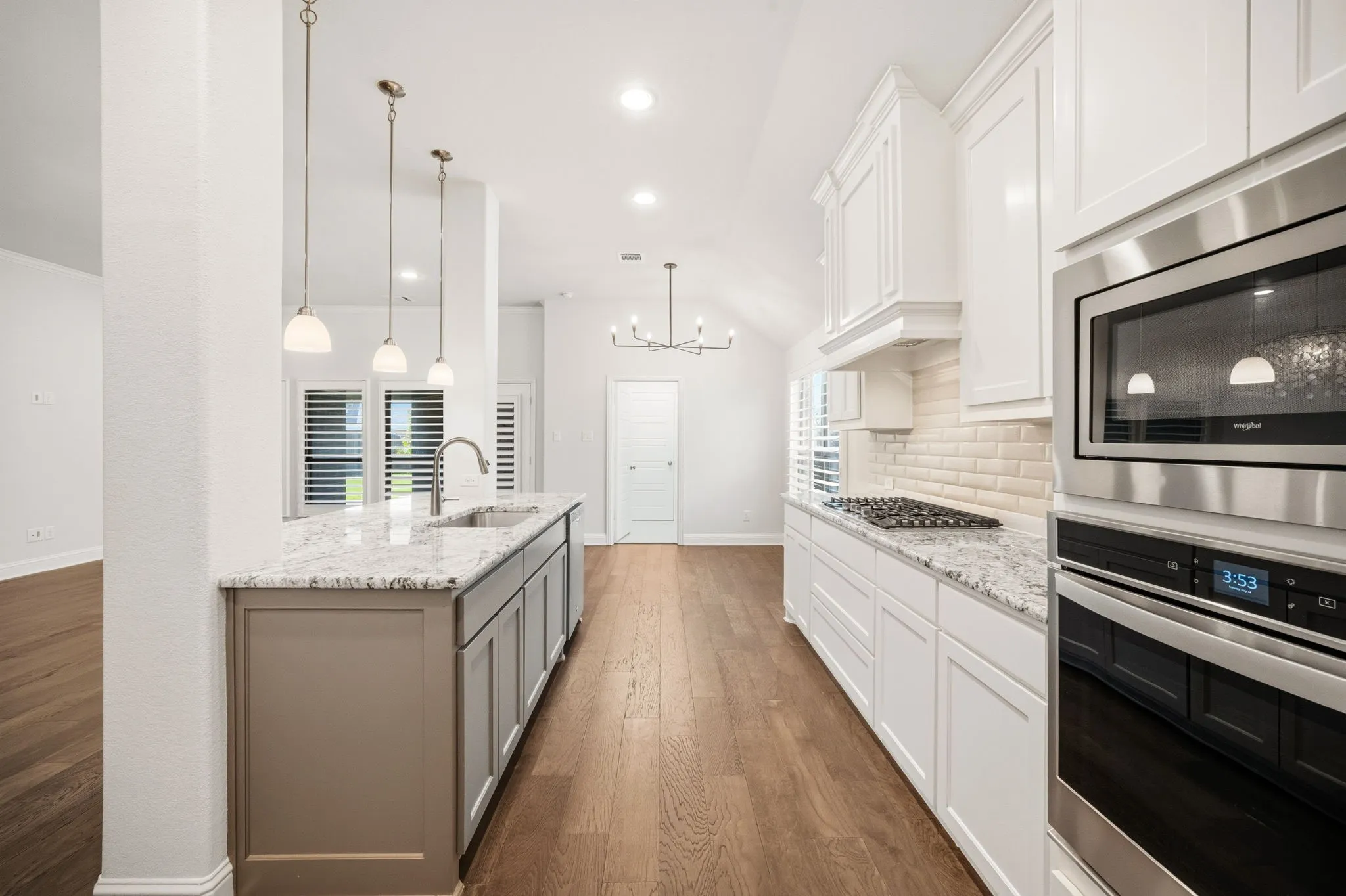 Gourmet kitchen featuring a gray island with a stainless steel sink, white perimeter cabinetry, stainless steel appliances, and wood-finish flooring
