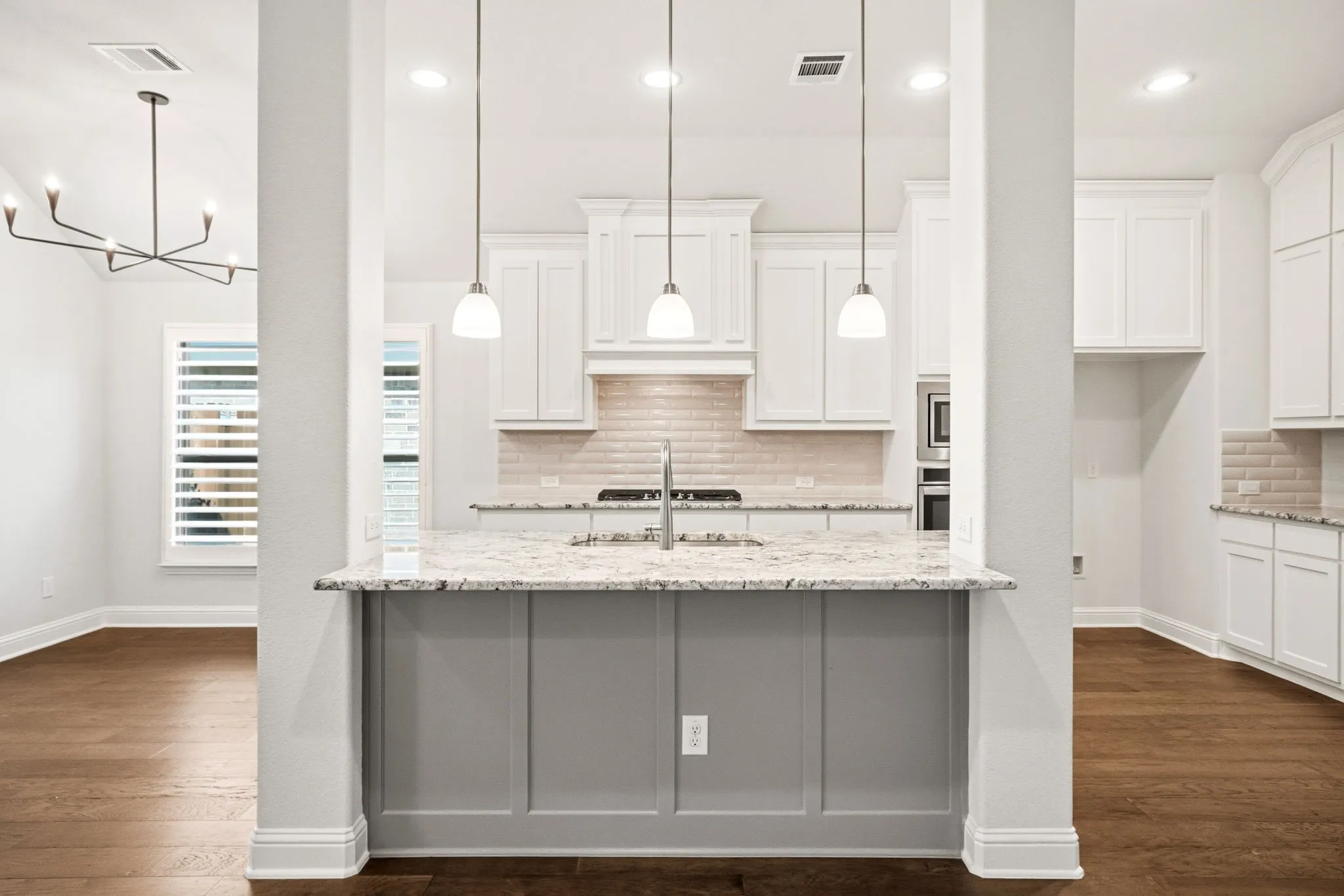Kitchen featuring a large island with three pendant lights, white cabinetry, integrated stainless steel appliances, a light-toned tile backsplash, and wood-finish flooring