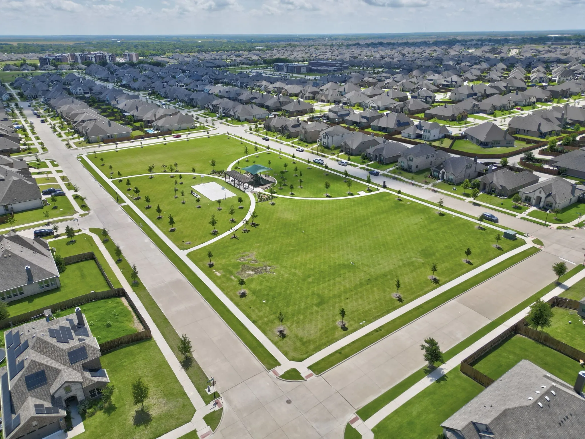 Expansive neighborhood park featuring a large green space, paved walking paths, a dedicated play area, and a shaded pavilion