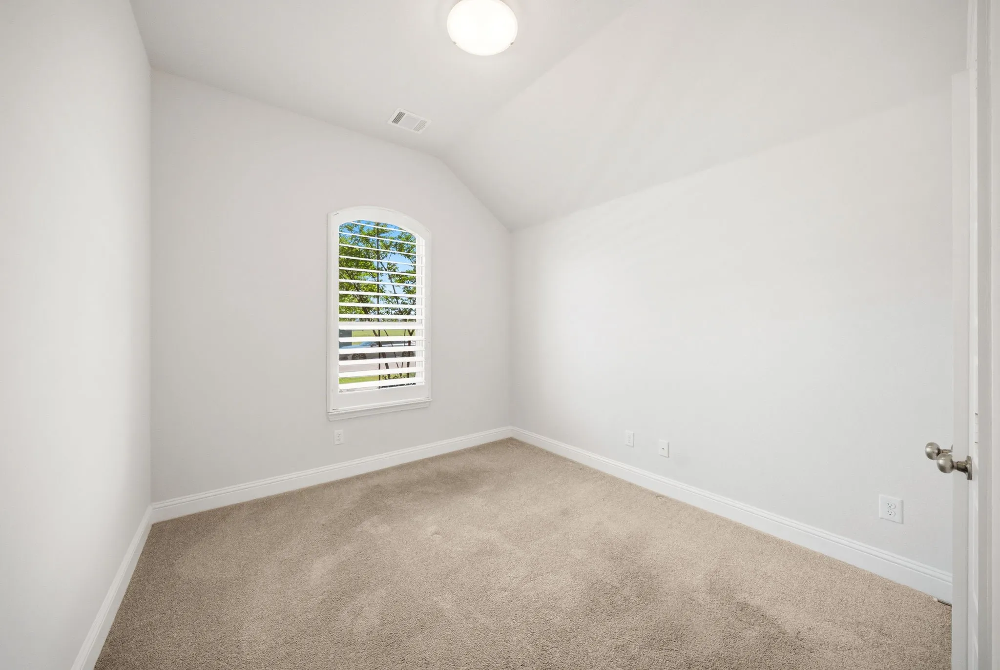 Arched window with louvered shutters, sloped ceiling, wood-finish desk, and floating wall shelves