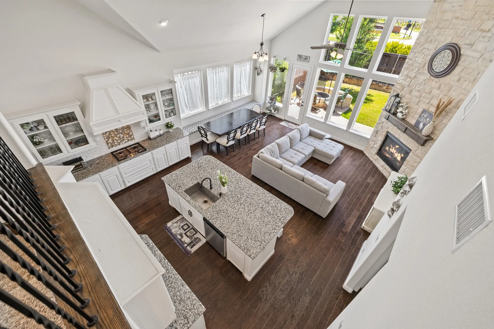 Open-concept living space featuring a vaulted ceiling with exposed beams, rich wood-finish flooring, and a floor-to-ceiling stone fireplace