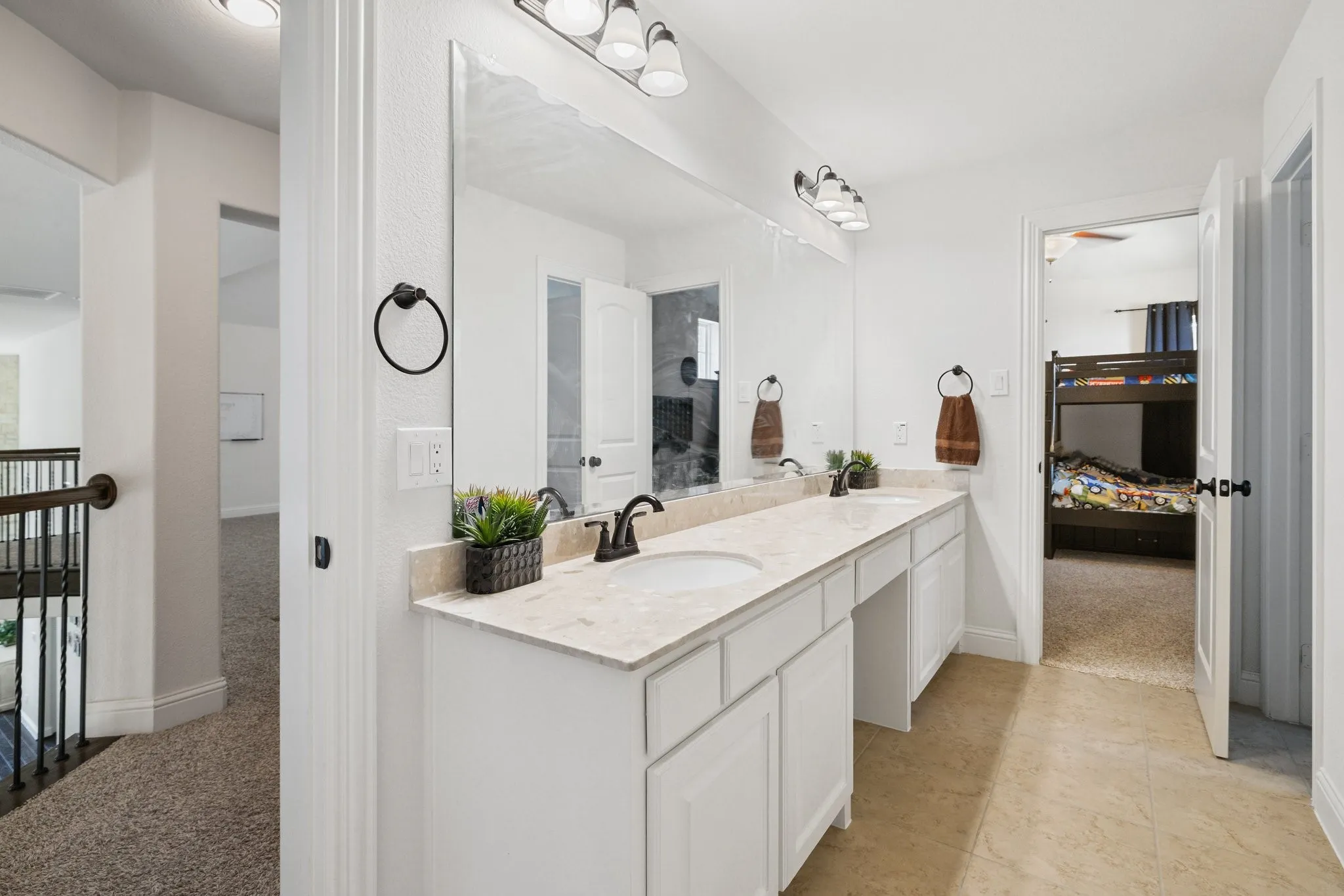 Bathroom featuring a double vanity with undermount sinks, light-toned countertop, white cabinetry, and a large wall-mounted mirror
