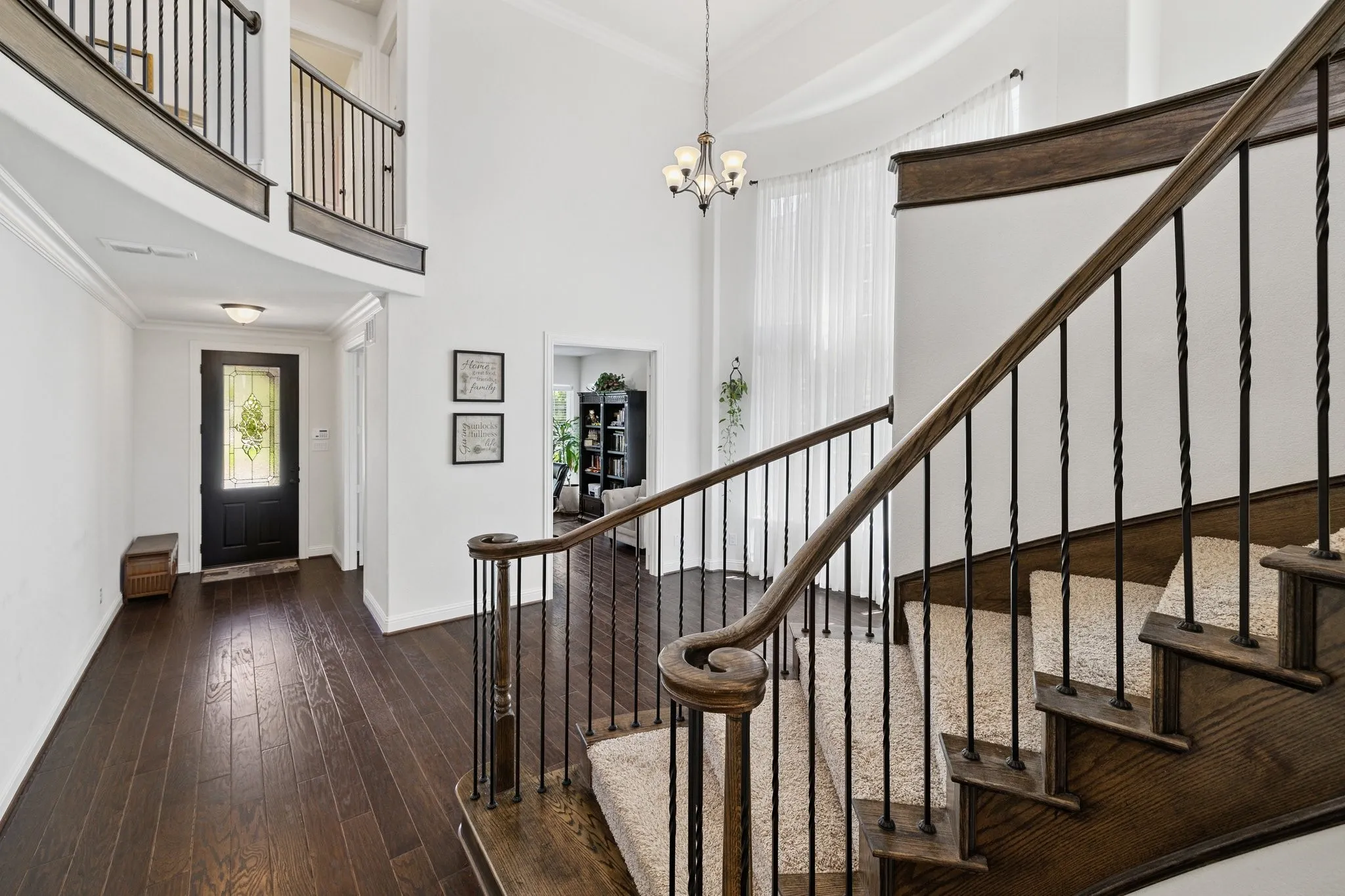 Two-story foyer featuring dark wood-finish flooring, a grand staircase with carpeted treads and wrought iron balusters, a curved upper landing, and a decorative chandelier