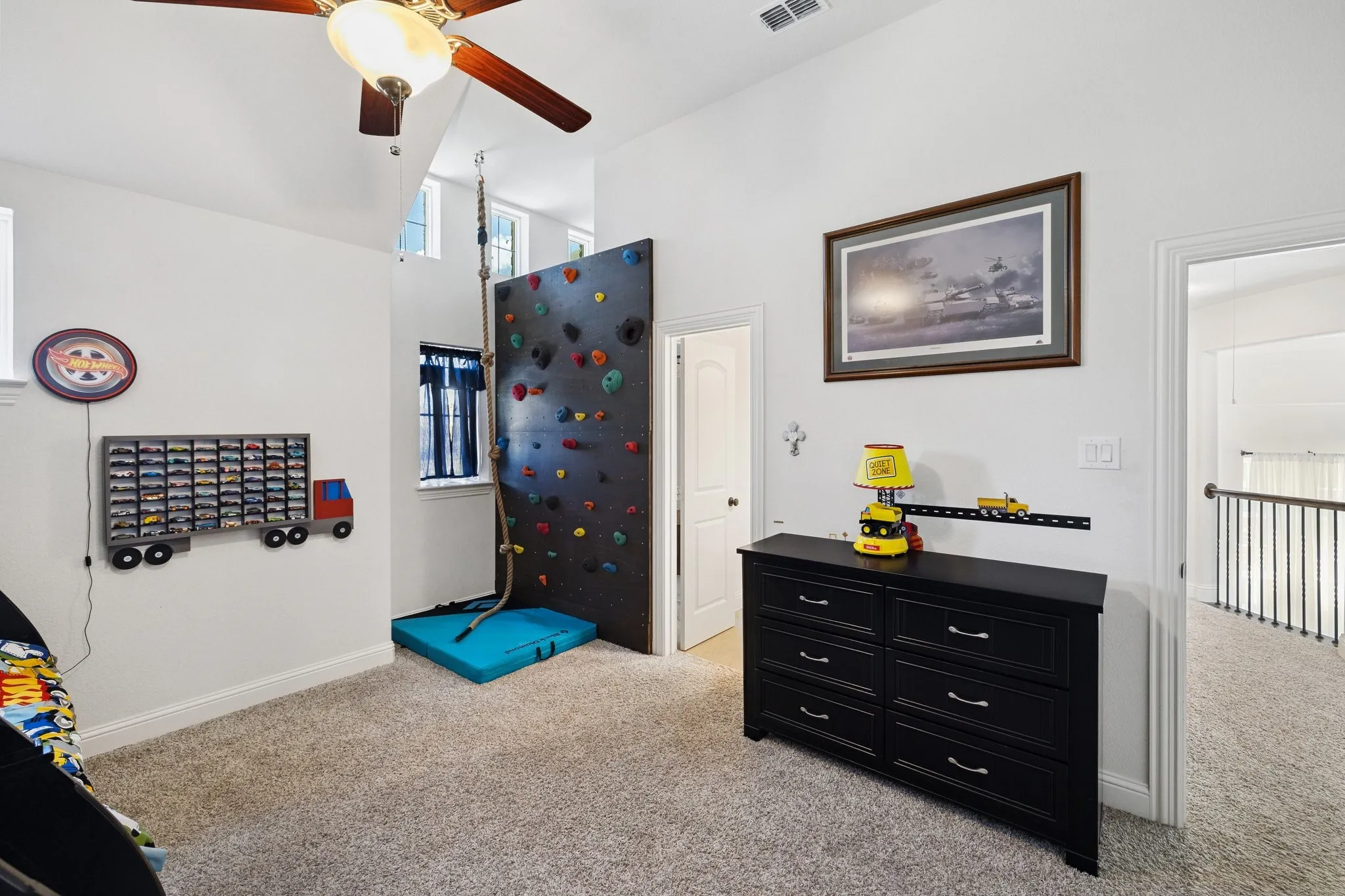Carpeted room featuring a ceiling fan with integrated lighting, a climbing wall with a safety mat, and a window with blinds
