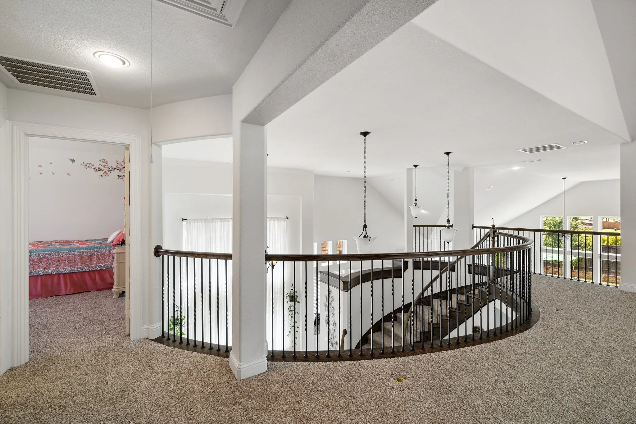 Carpeted upper-level hall featuring a curved wrought iron railing overlooking the lower level
