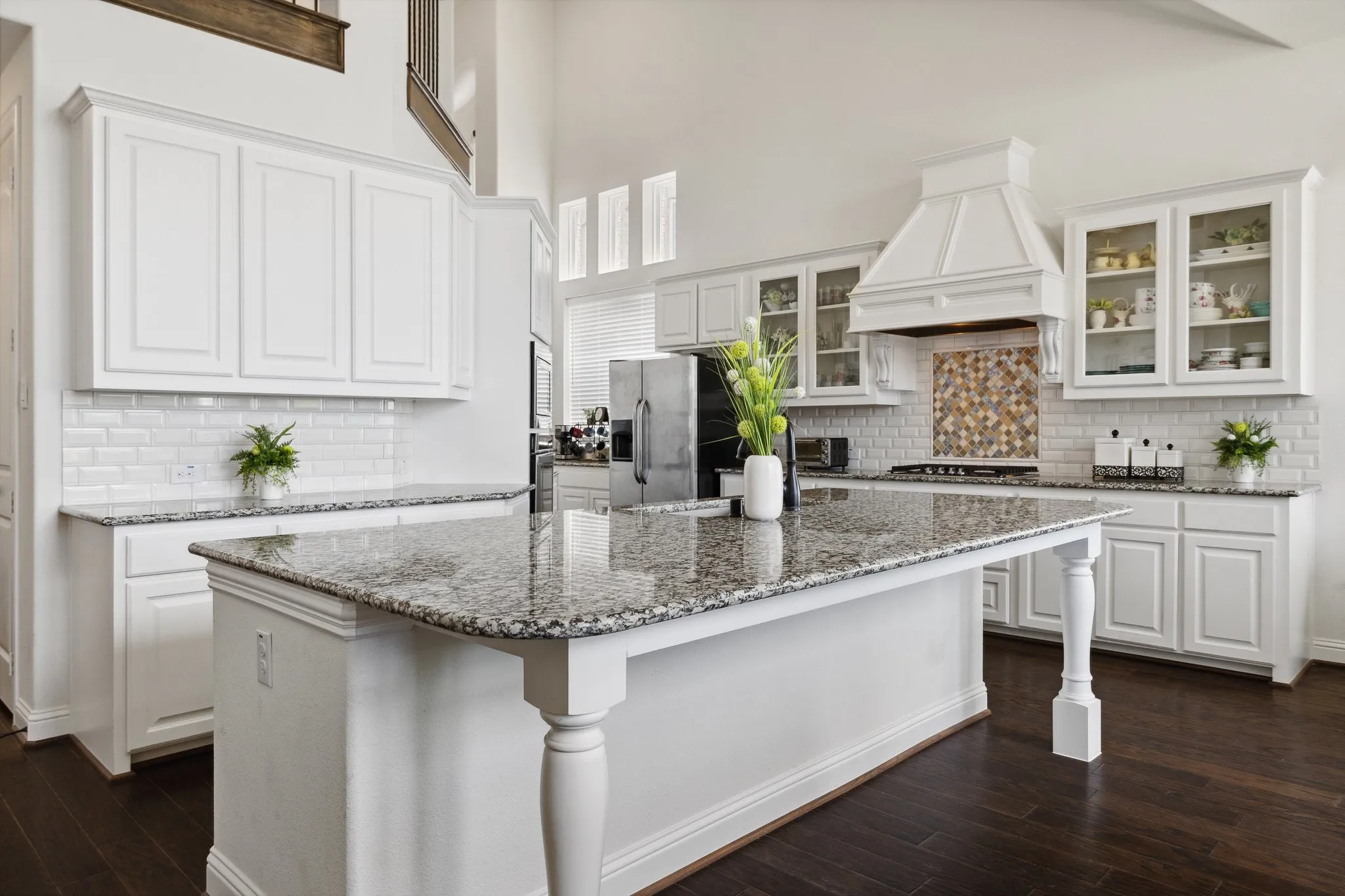 Kitchen featuring a central island with a granite countertop and turned legs, white cabinetry, subway tile backsplash, and dark wood-finish flooring
