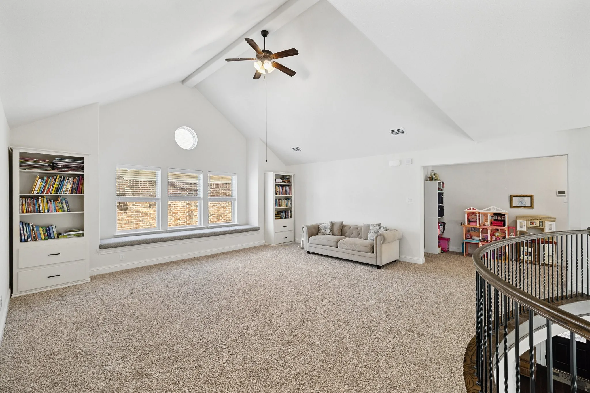 Spacious carpeted bonus room featuring a vaulted ceiling with exposed beam, ceiling fan, and built-in shelving units