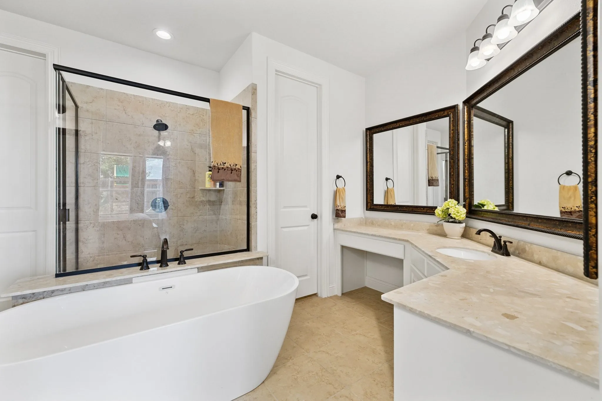 Bathroom featuring a freestanding soaking tub, a frameless glass shower with black trim, a dual vanity with light-toned countertops, and two framed mirrors