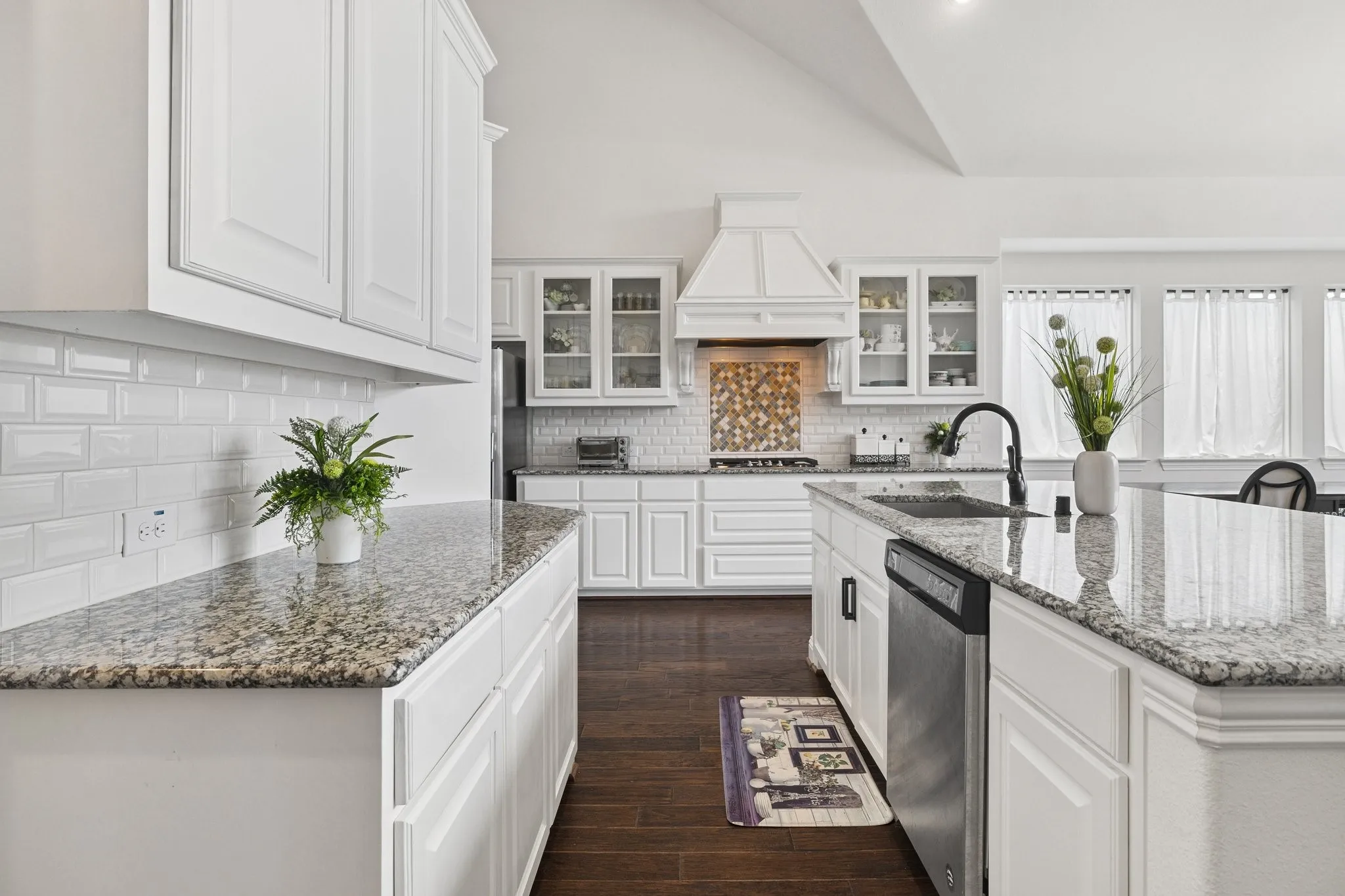 Spacious kitchen featuring white cabinetry, granite countertops, subway tile backsplash, a large kitchen island with an integrated sink, and dark wood-finish flooring