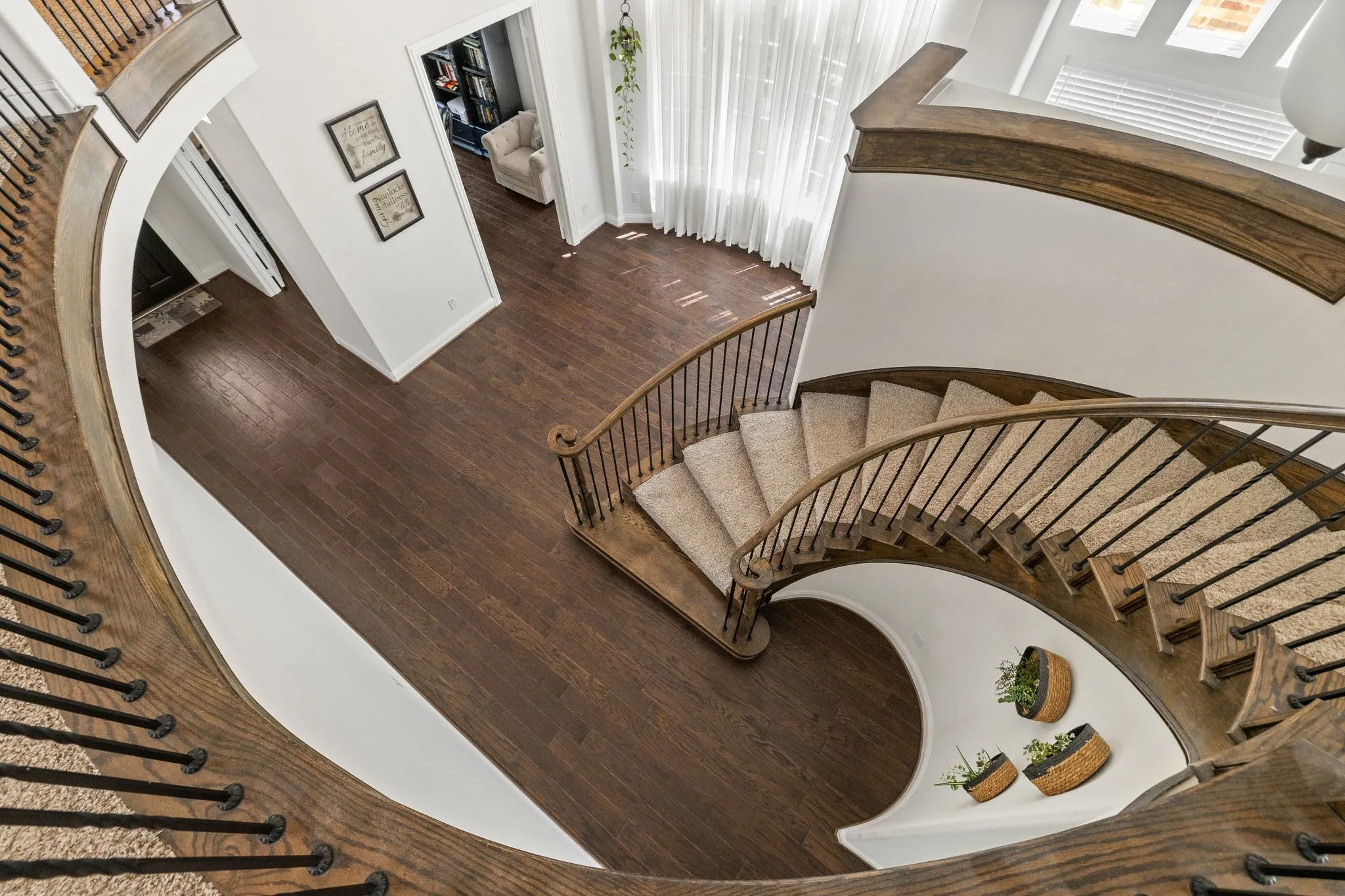 Grand curved staircase featuring wood-finish treads and risers with carpet runners, wrought iron balusters, and a rich wood-finish handrail