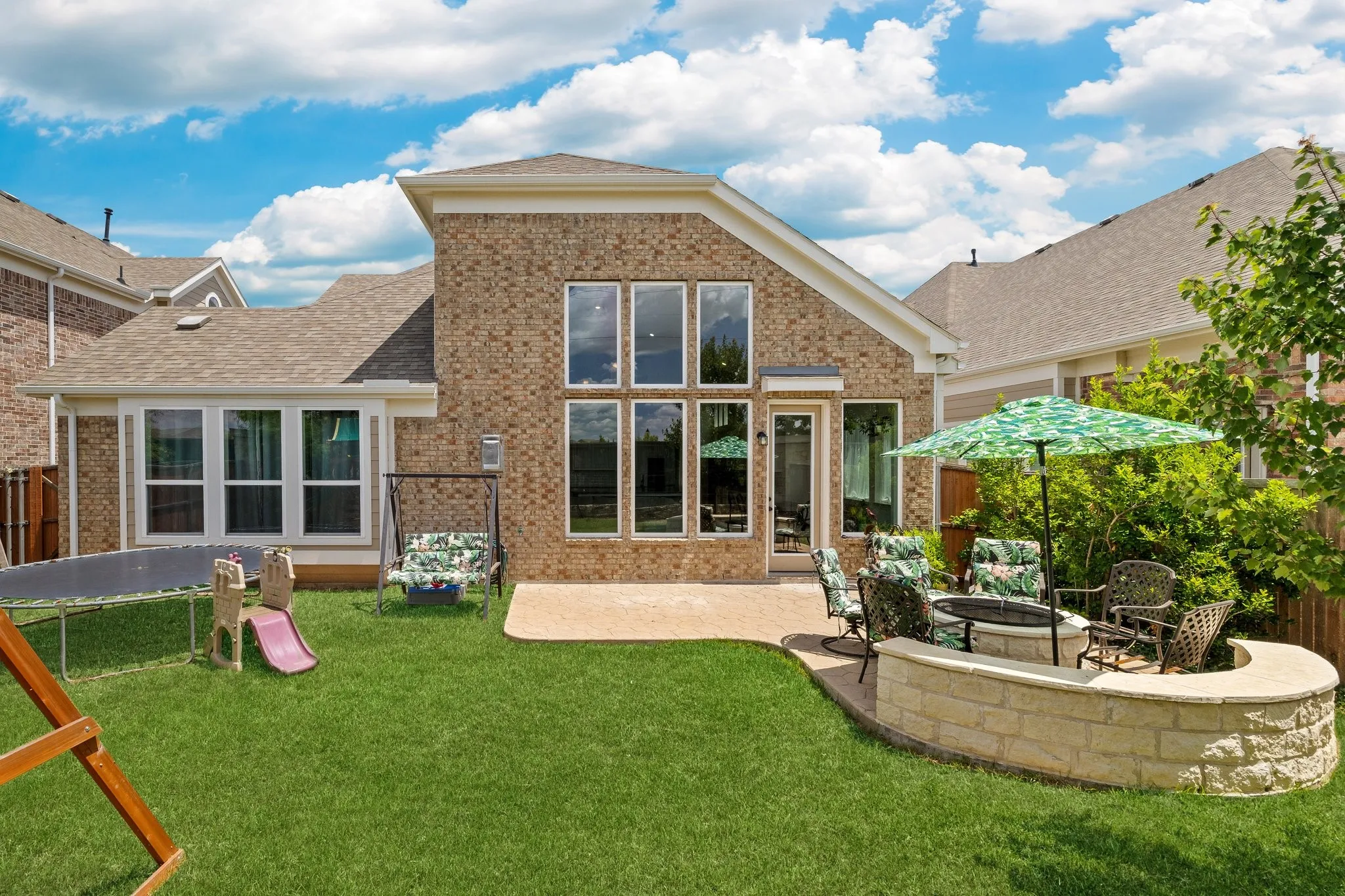 Spacious backyard featuring a manicured lawn, an extended patio area, and a built-in stone fire​​‌​​​​‌​​‌‌​‌‌​​​‌‌​‌​‌​‌​​​‌​​ pit