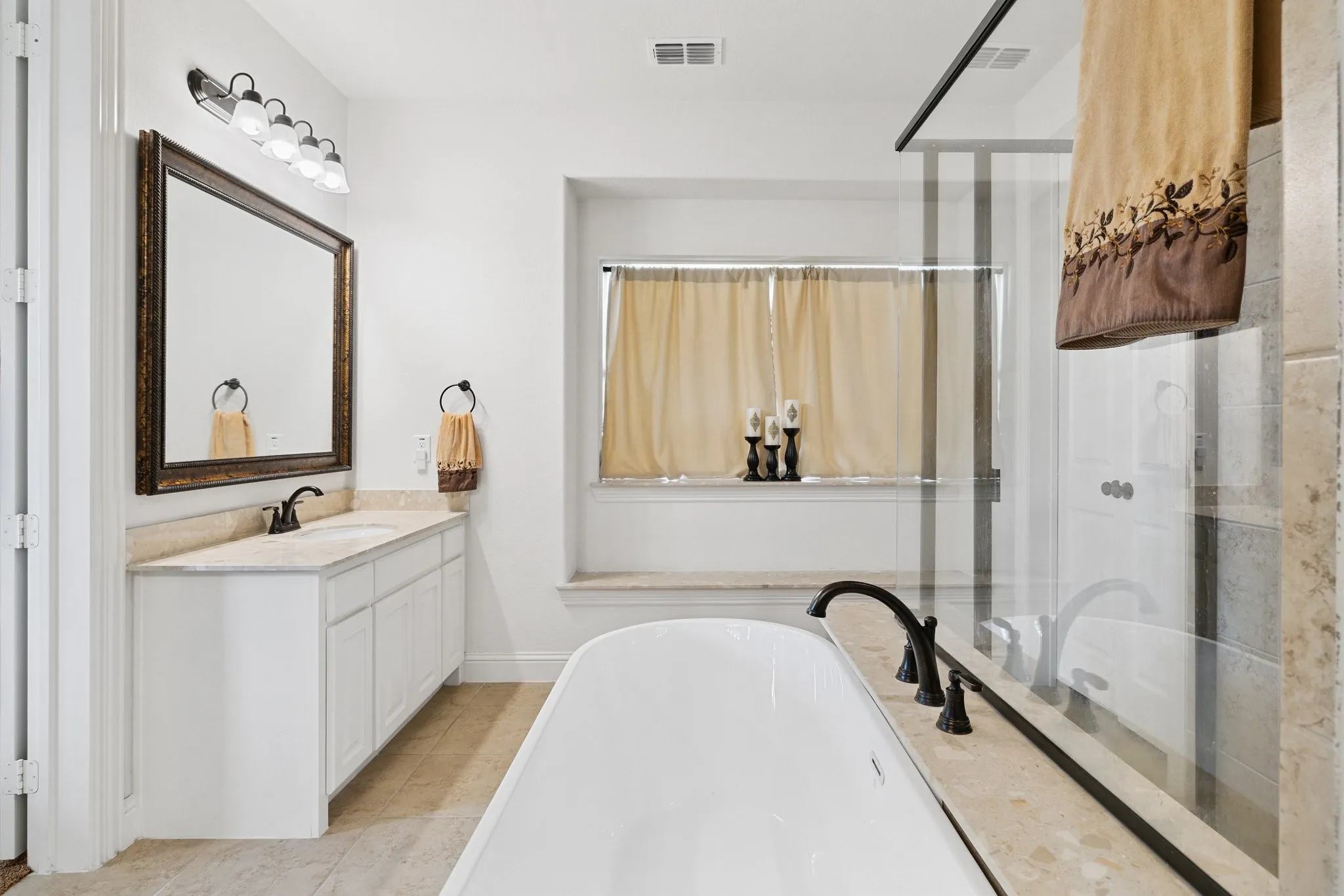 Freestanding bathtub with black fixtures, glass-enclosed shower, and a white vanity with a stone countertop