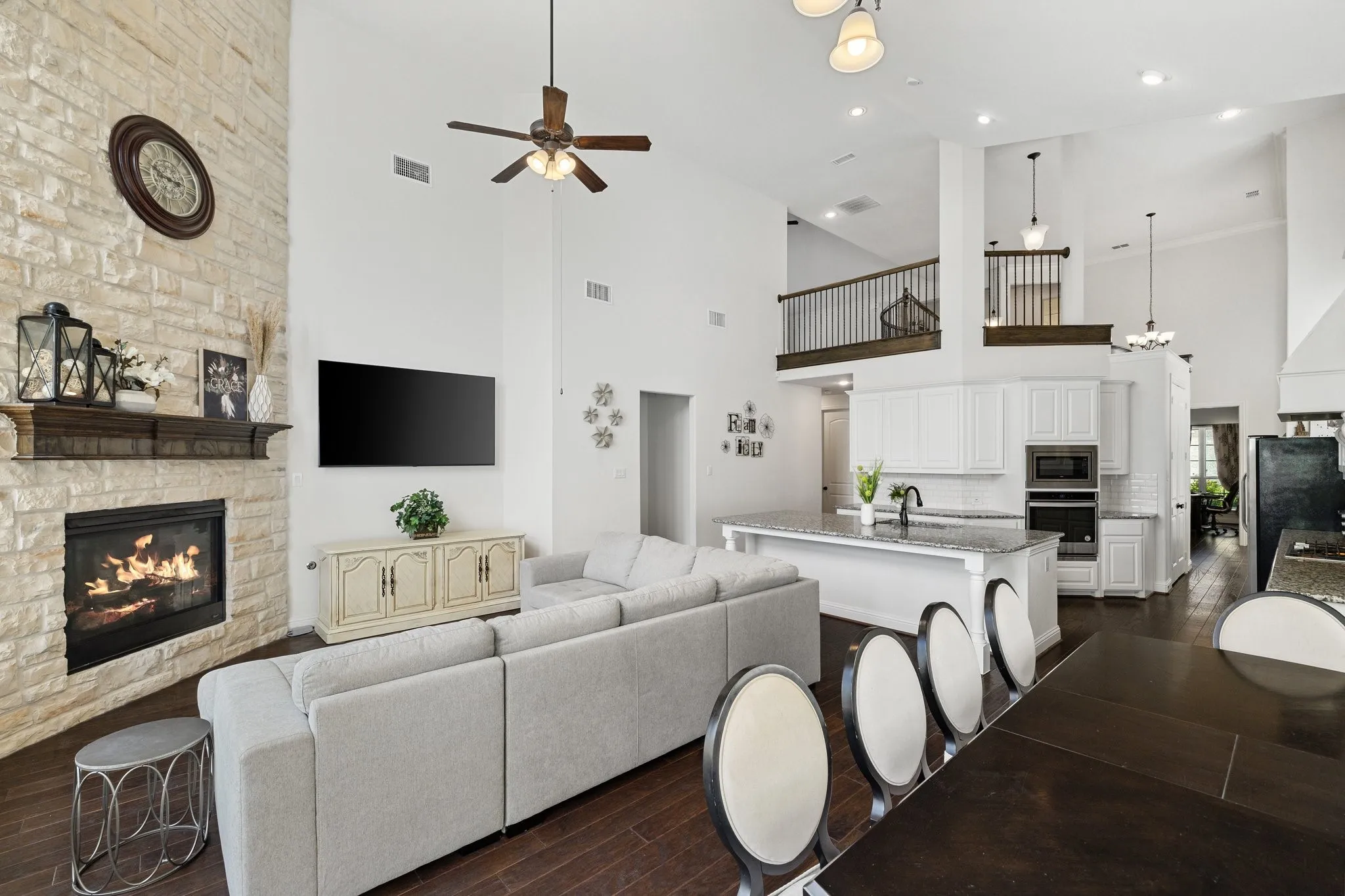 Open-concept living area featuring a stacked stone fireplace with a wood mantel, high vaulted ceilings, and dark wood-finish flooring