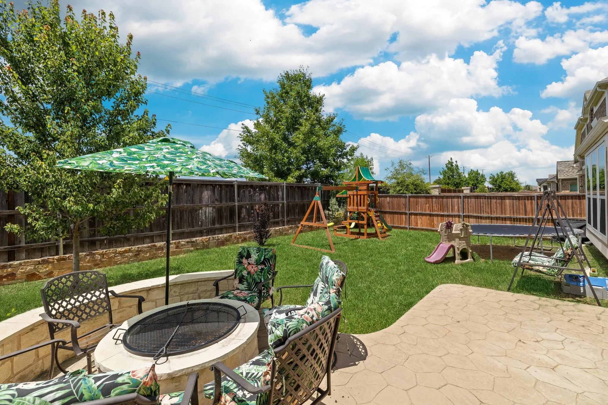 Expansive backyard featuring a stone patio, built-in stone fire pit, and privacy fencing