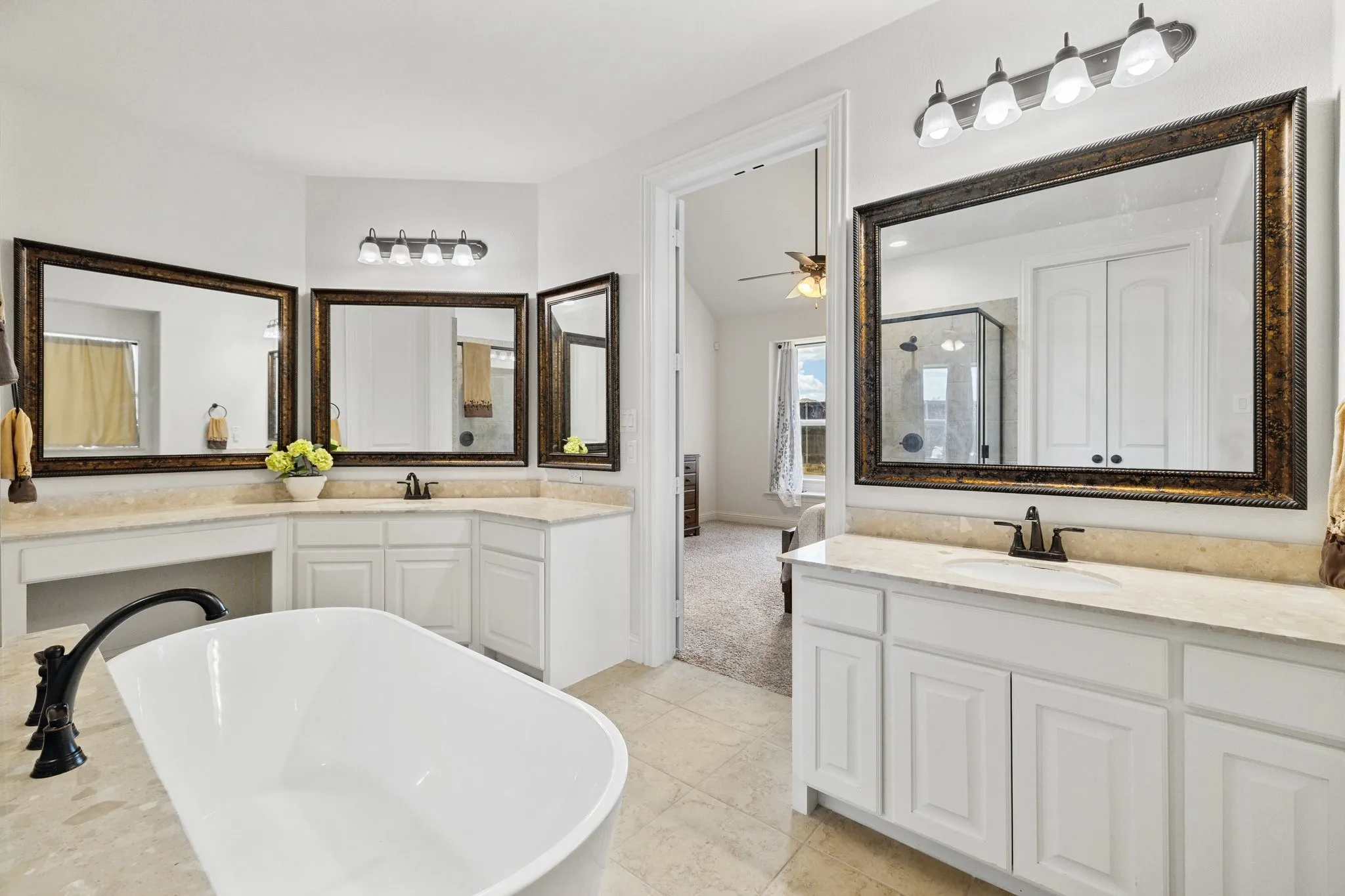 Bathroom featuring a freestanding tub with a matte black faucet, dual vanities with light-toned countertops, white cabinetry, and large framed mirrors