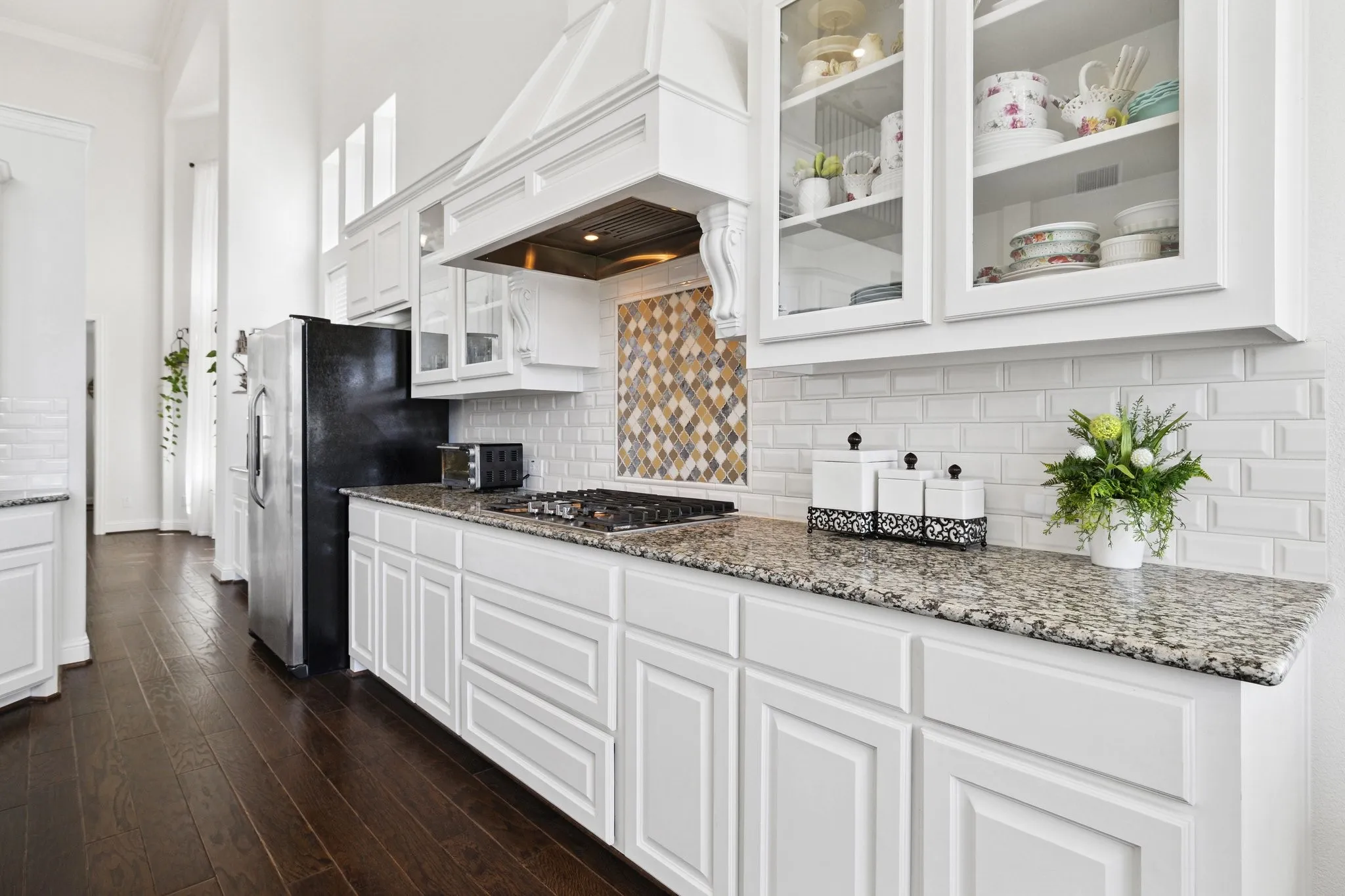 Kitchen featuring white shaker-style cabinetry, a built-in gas range, a decorative range hood, light-colored granite countertops, and a white subway tile backsplash