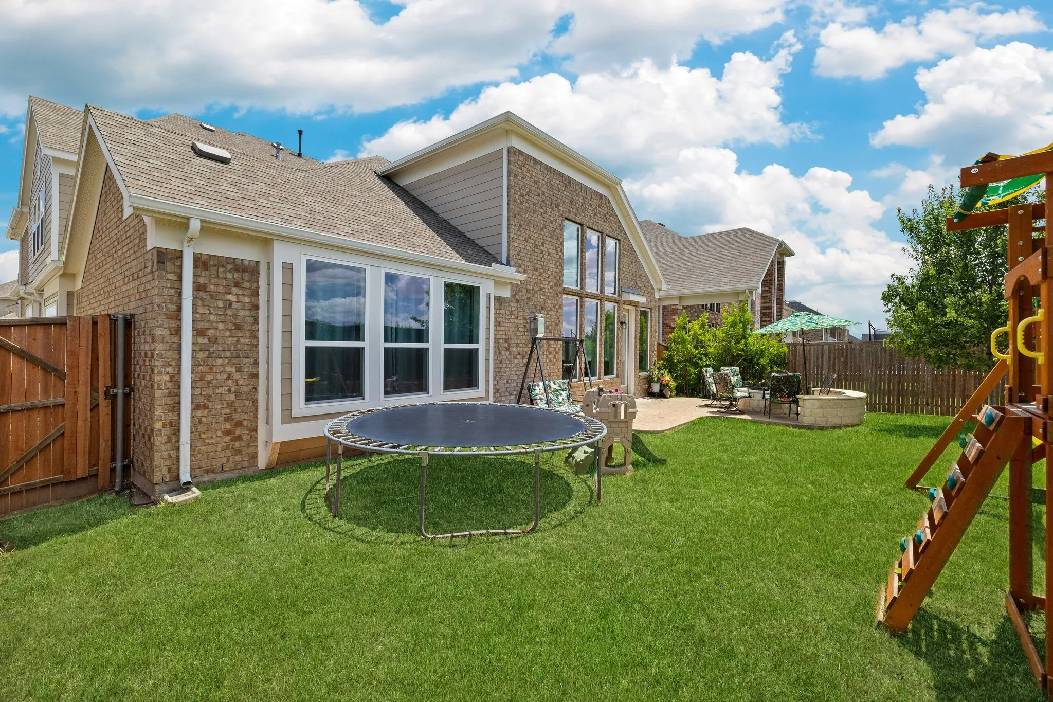 Expansive fenced backyard featuring a manicured lawn, a concrete patio, and a built-in fire pit