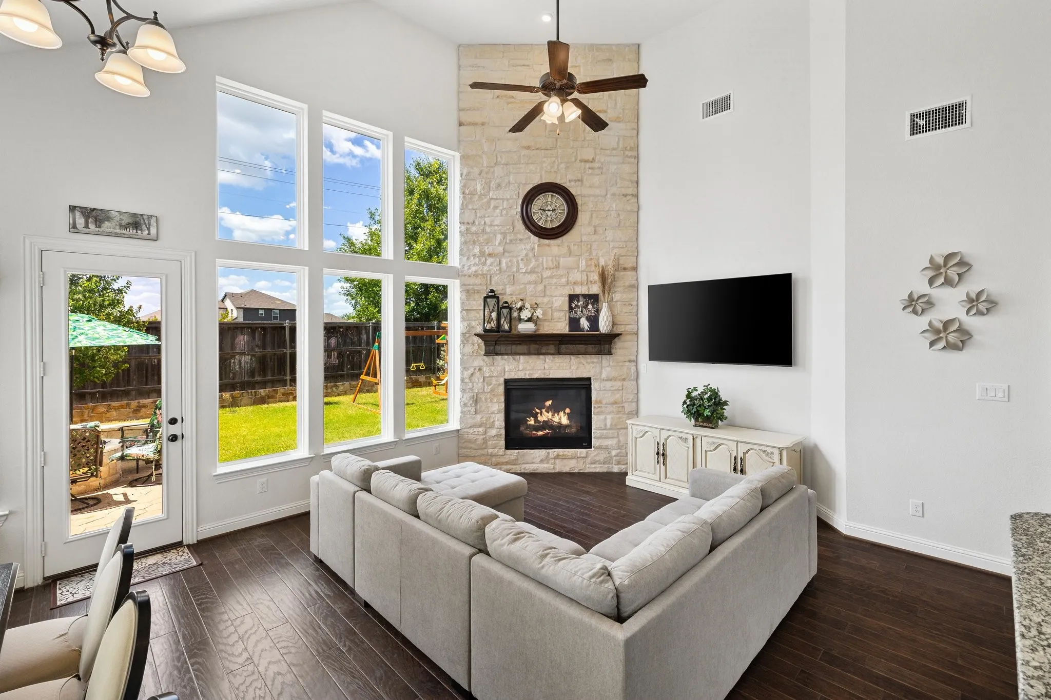 Vaulted ceiling living area featuring a stone-clad fireplace with a wood mantel, wood-finish flooring, and a ceiling fan