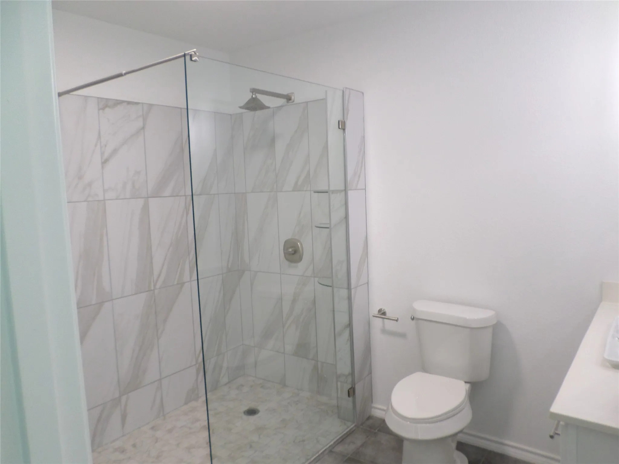Glass-enclosed shower with large format tile surround and rainfall showerhead