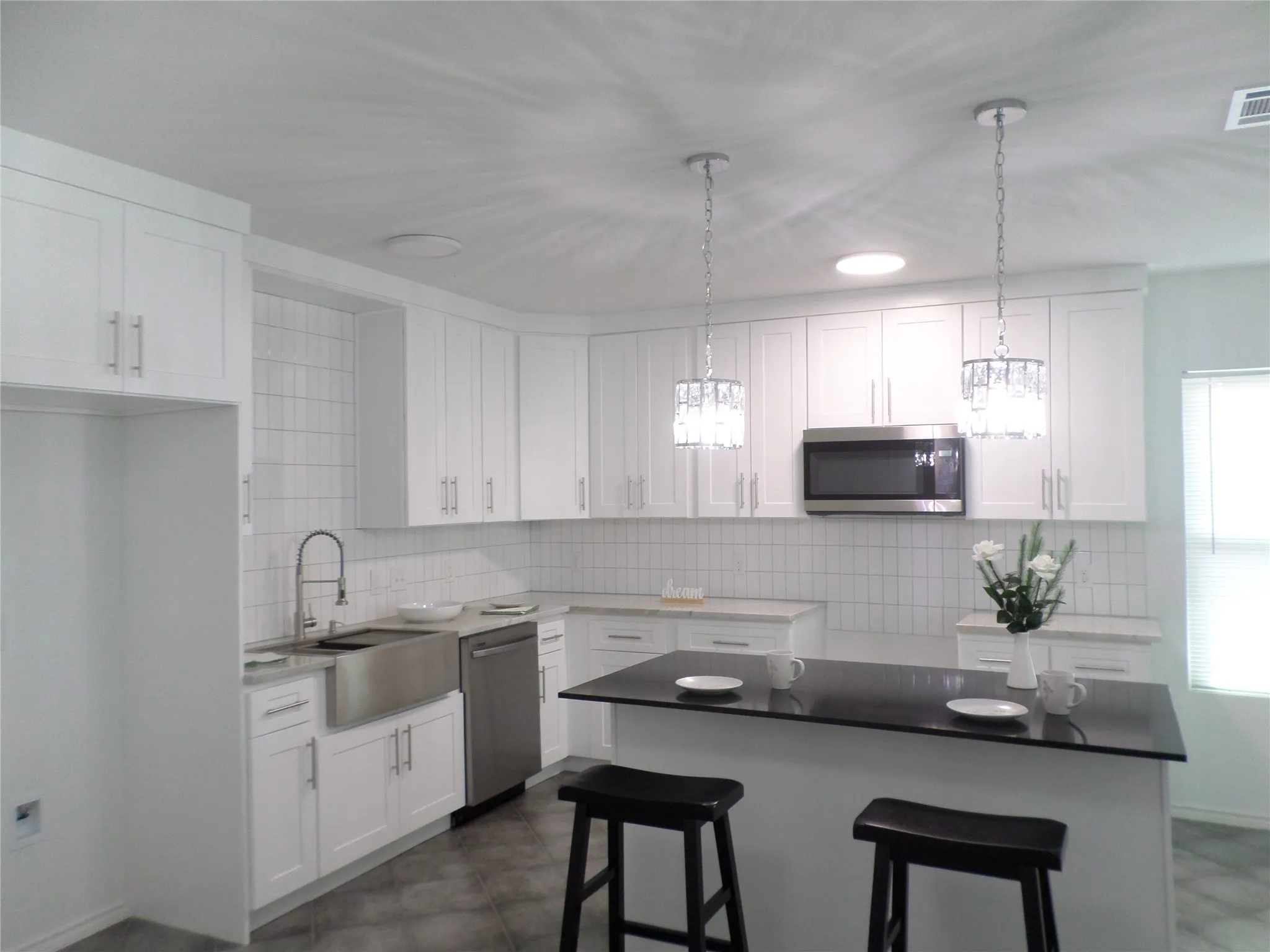Kitchen featuring white cabinetry, stainless steel appliances, a farmhouse sink, subway tile backsplash, and a central island with a dark countertop