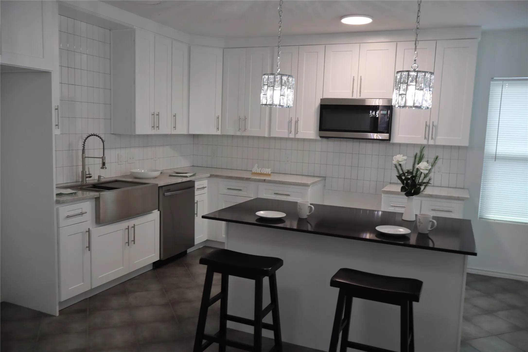 Modern kitchen featuring white shaker cabinetry, stainless steel appliances, a farmhouse sink, subway tile backsplash, and a dark countertop island