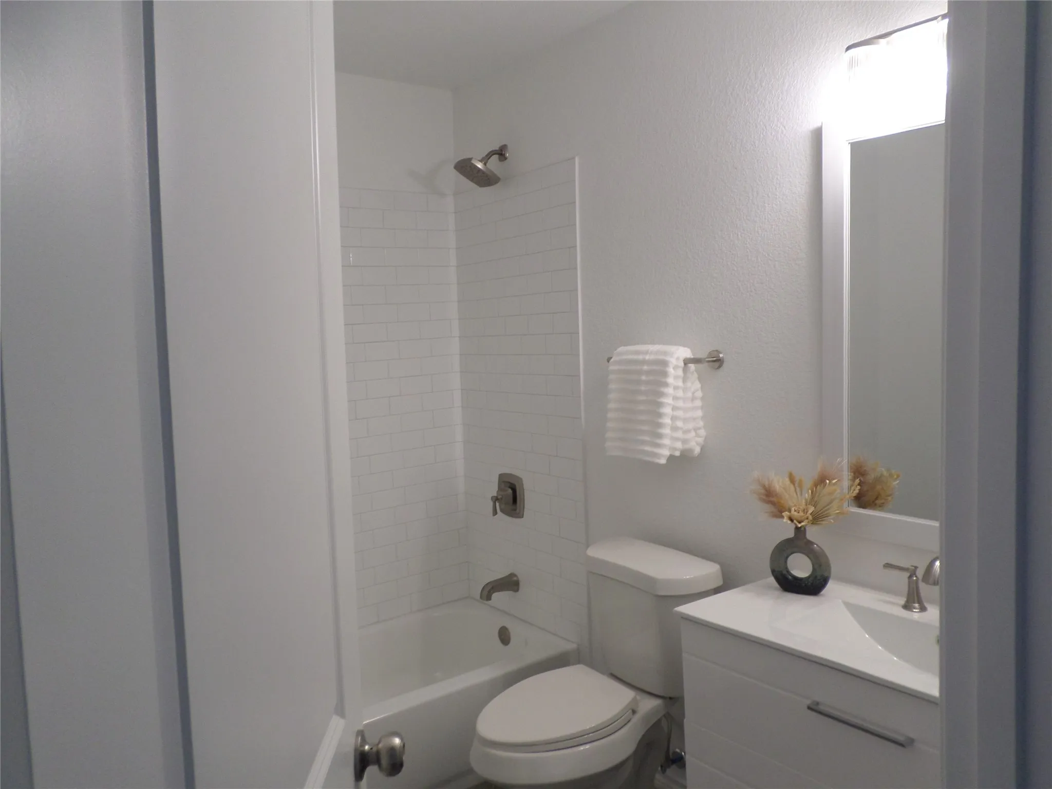 Bathroom featuring a white subway tile shower surround, brushed nickel shower fixtures, a white vanity with a single sink, and a framed mirror with overhead lighting