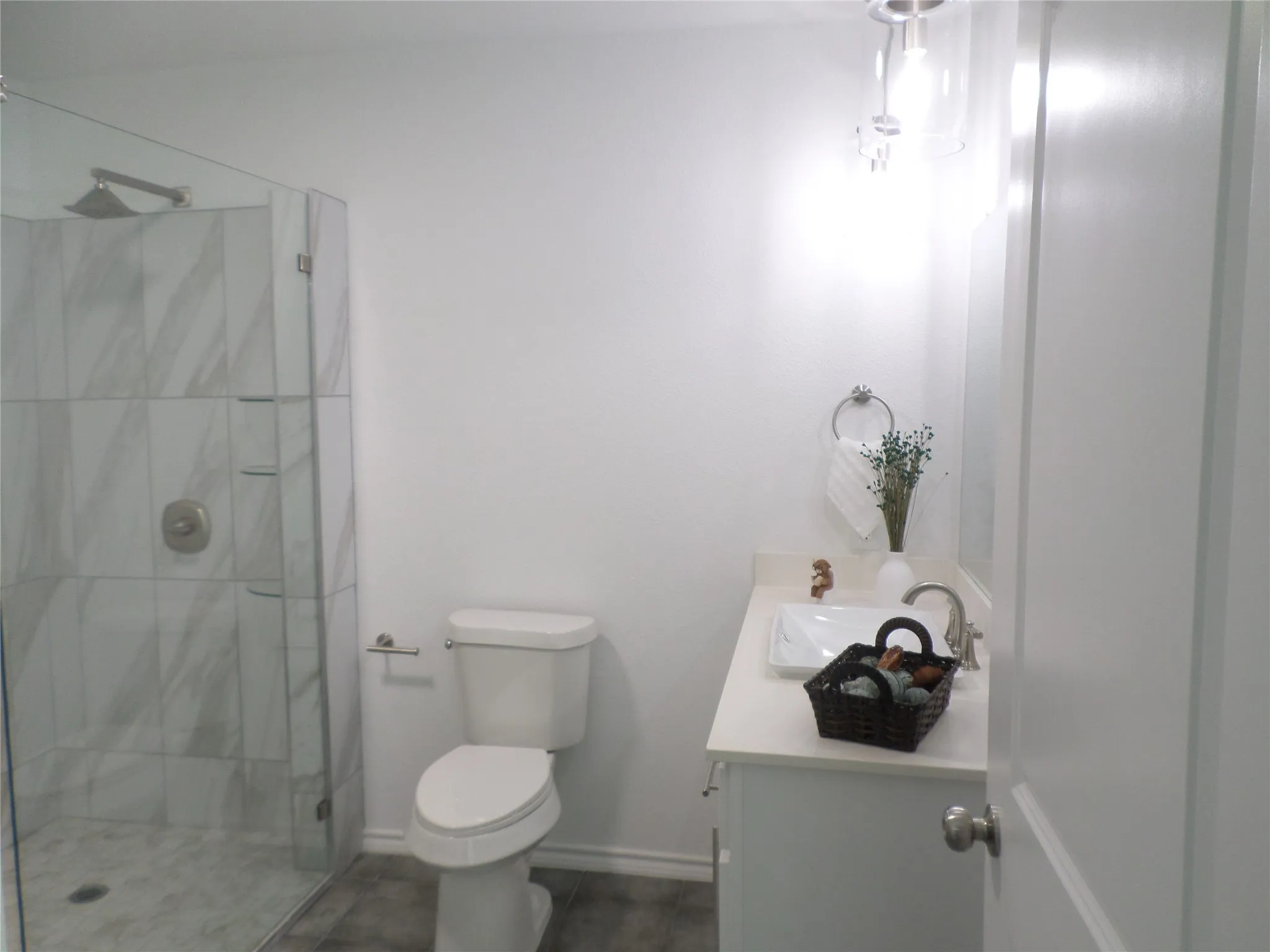 Contemporary bathroom featuring a glass-enclosed shower with large format white and grey-veined tile, a rainfall showerhead, and a built-in shelf